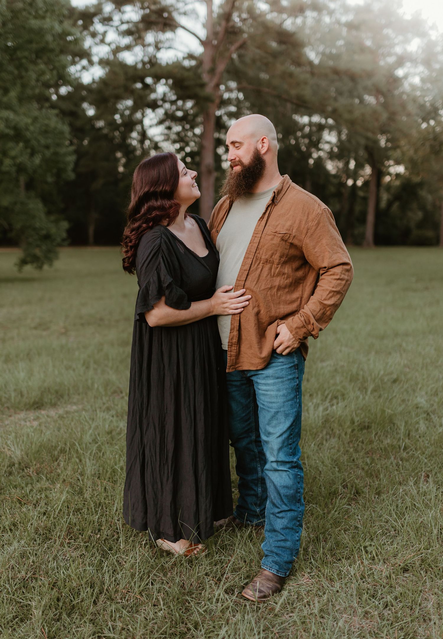 A couple shares an intimate moment together in a grassy field at sunset wearing casual attire.