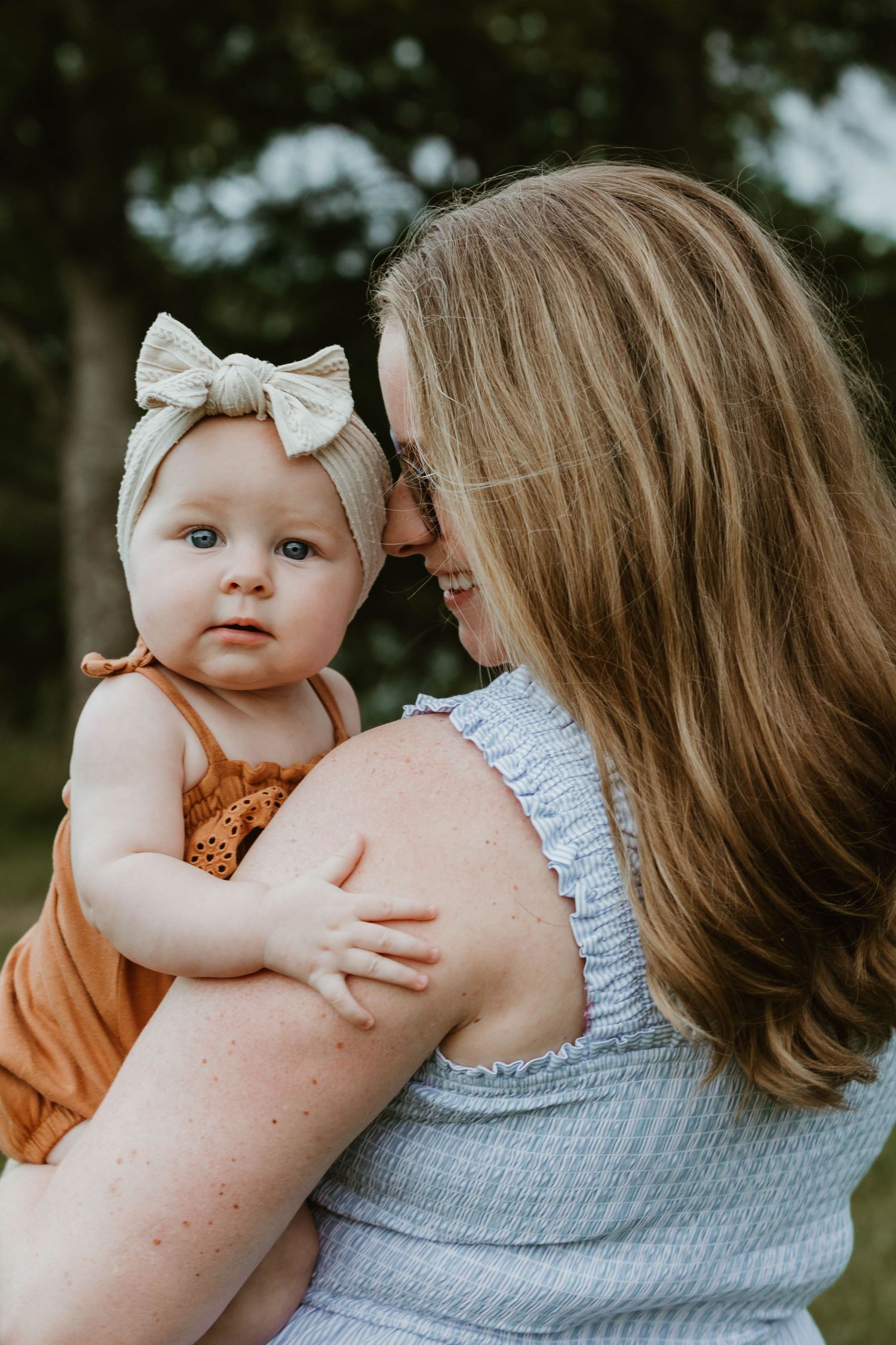 An intimate outdoor portrait of parent and baby wearing bow headband in summer setting.