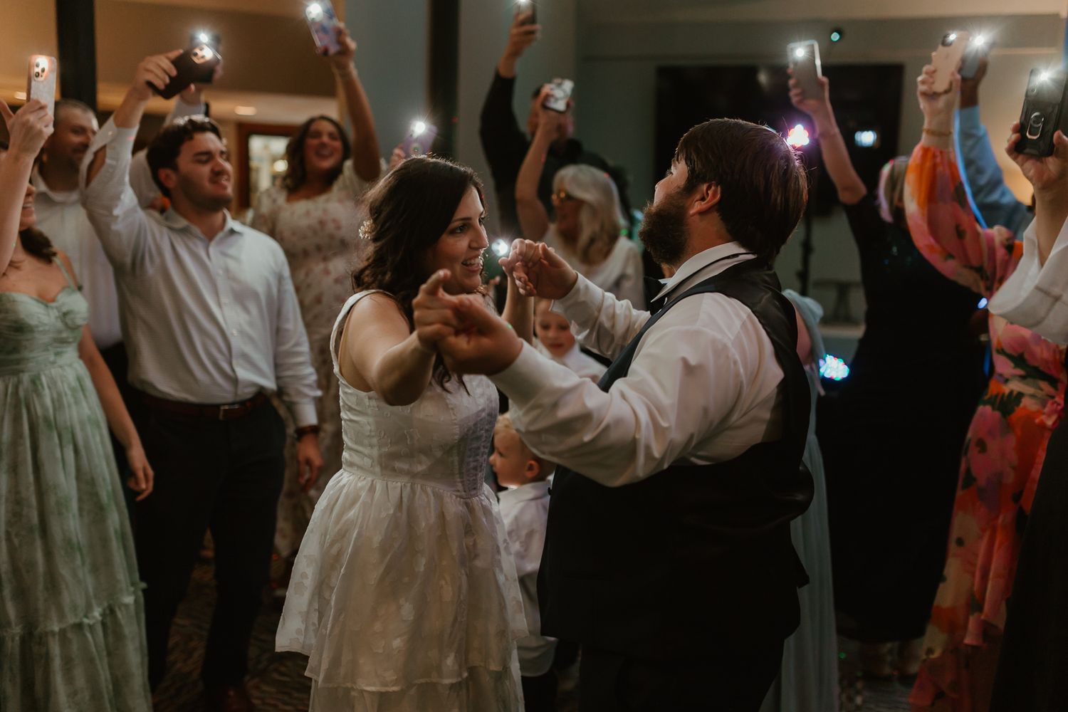 Wedding reception dance floor filled with celebrating guests under dim lighting.