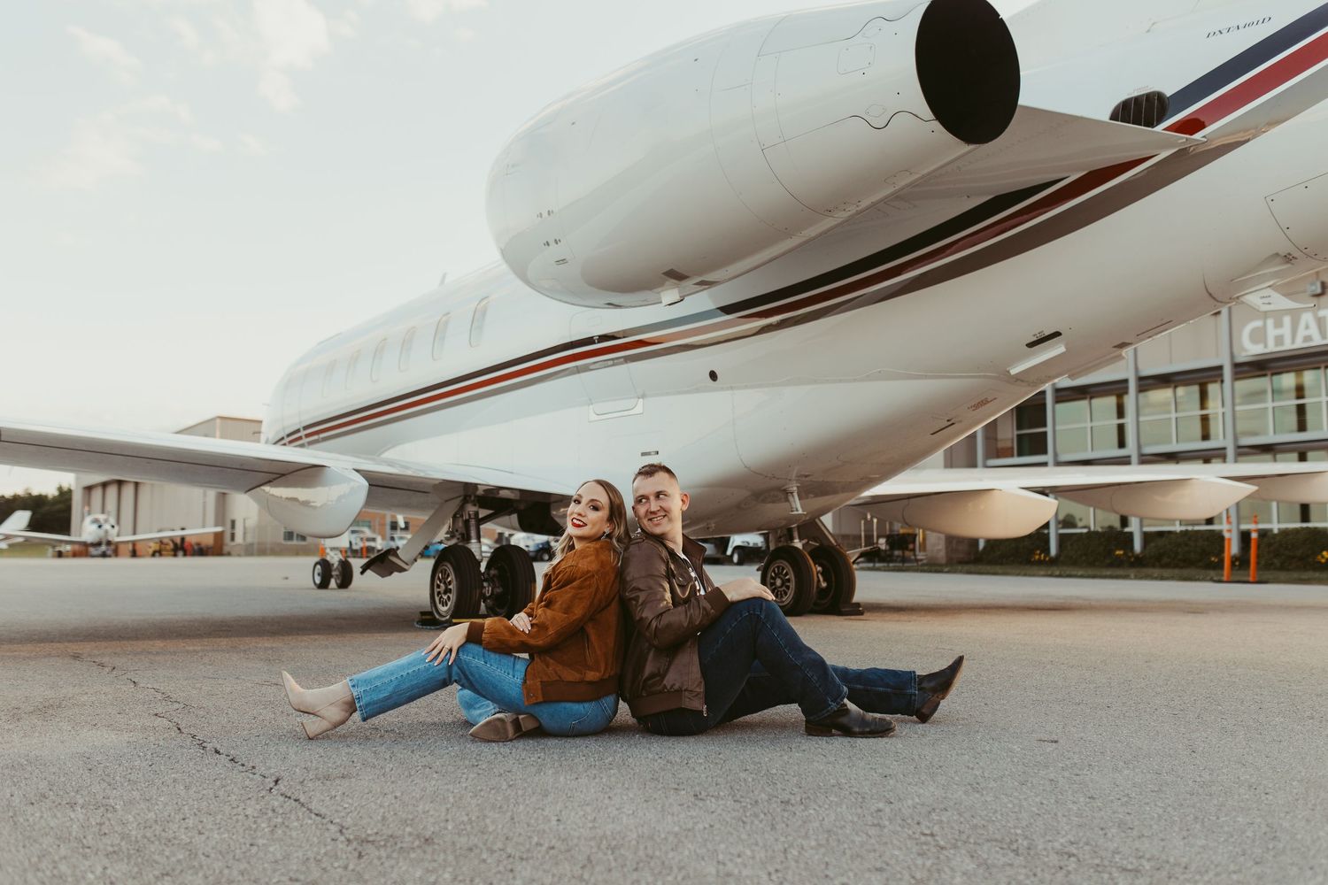 Two people in casual clothing lying on the ground next to a parked aircraft.