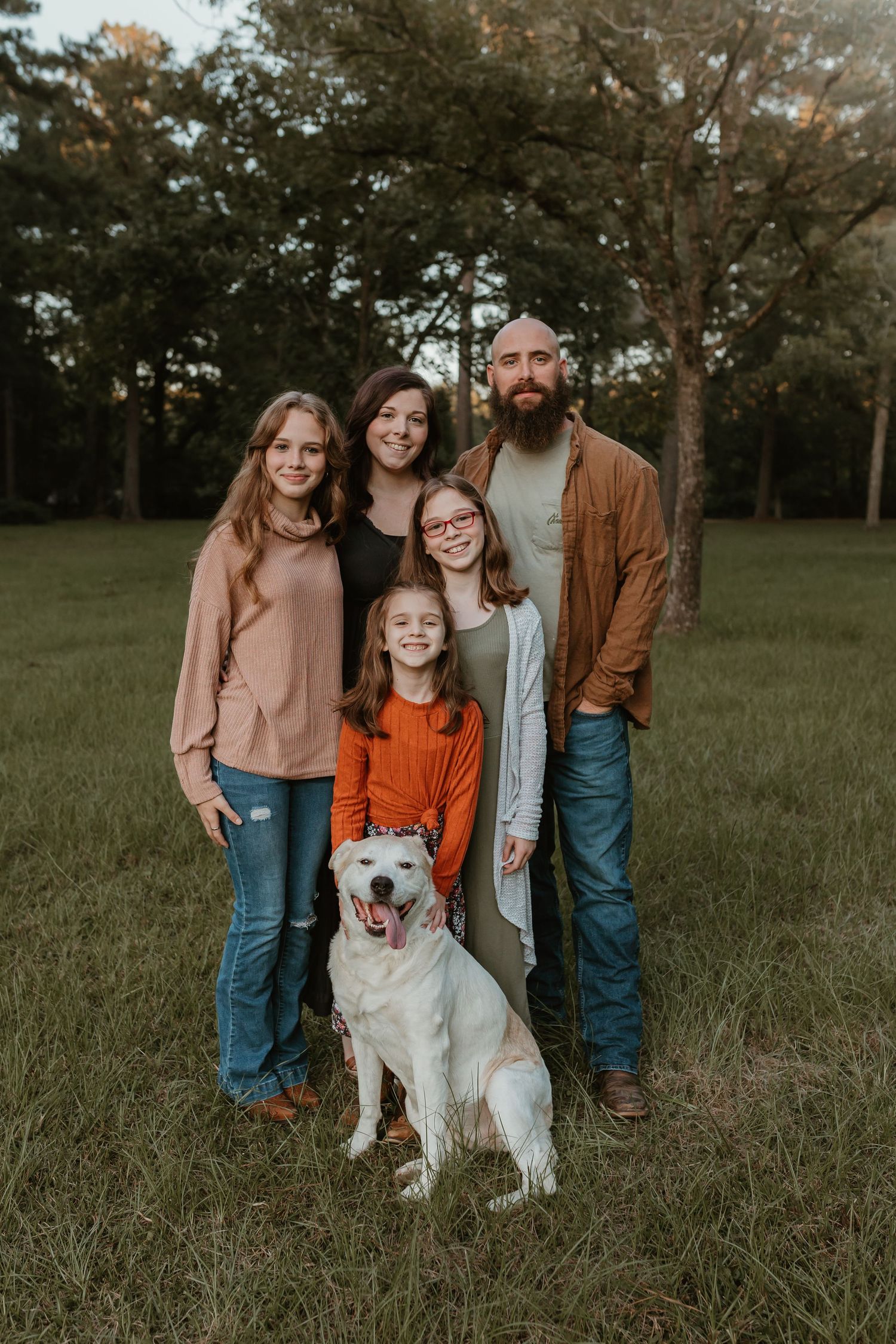 Family portrait with a happy white dog in a grassy field during golden hour.