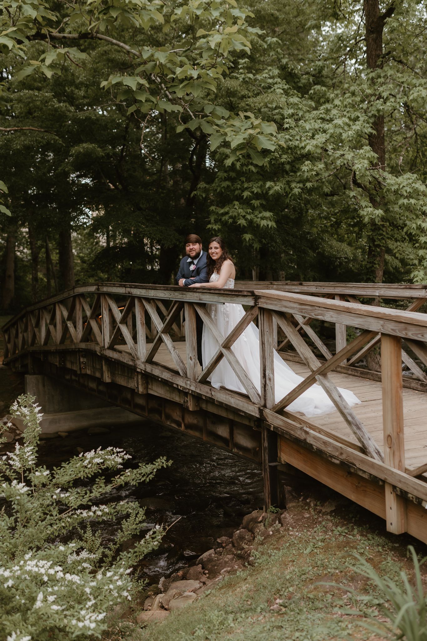 Romantic wedding photos captured on scenic wooden bridge in wooded setting.