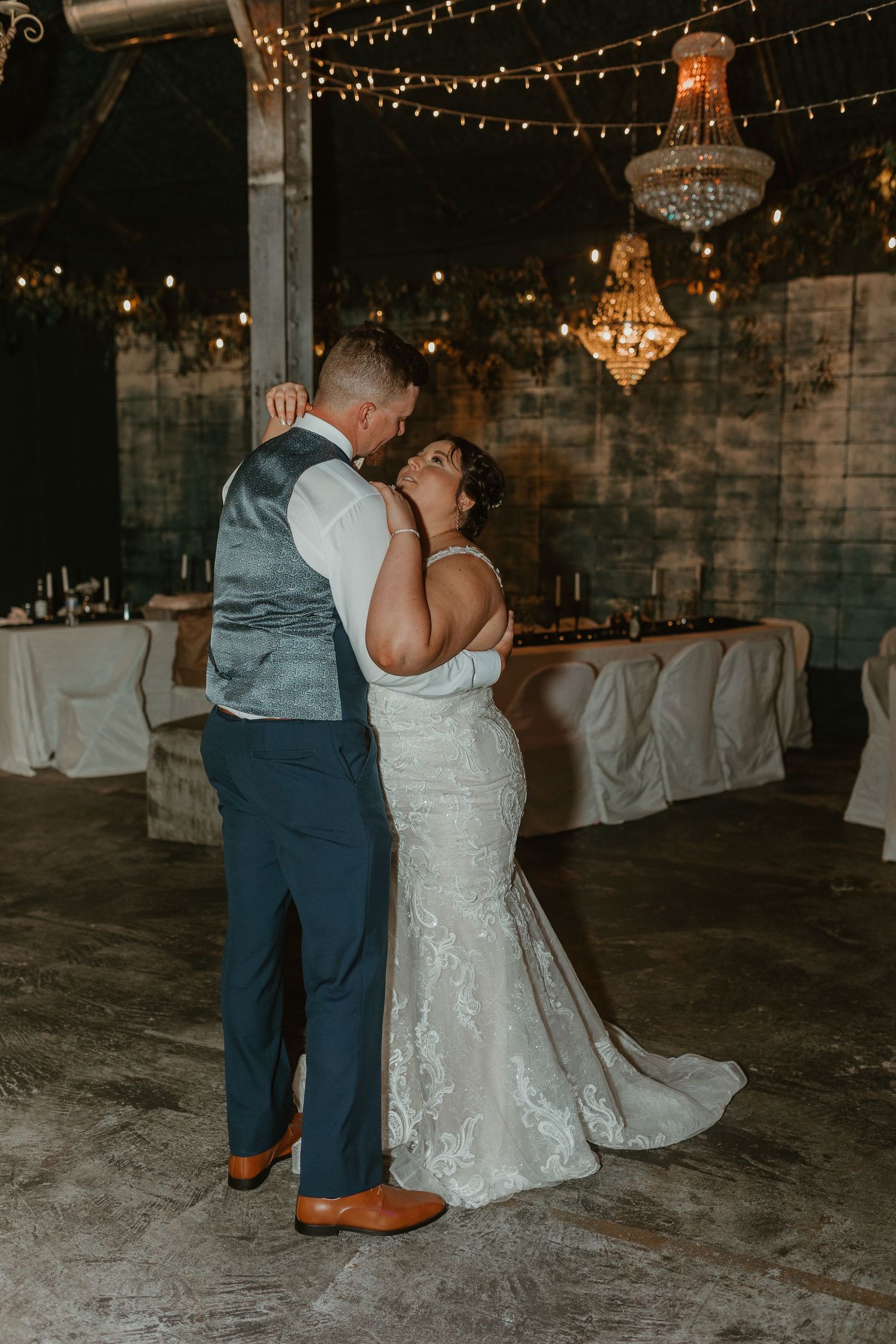 A romantic first dance moment under sparkling chandeliers at an industrial-style wedding venue.