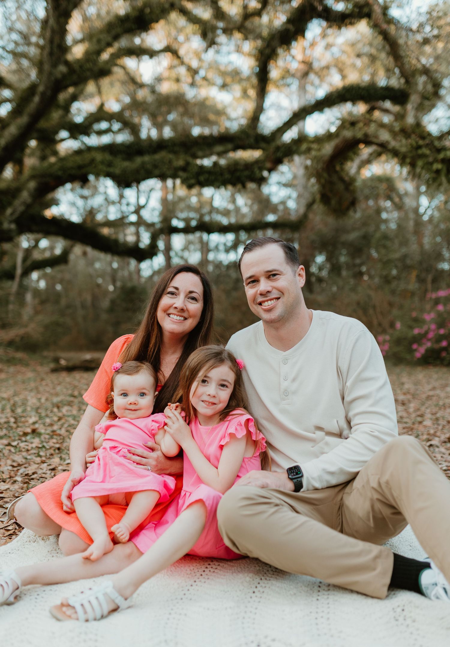Family lounging together on a blanket under a large oak tree during an outdoor photo session.