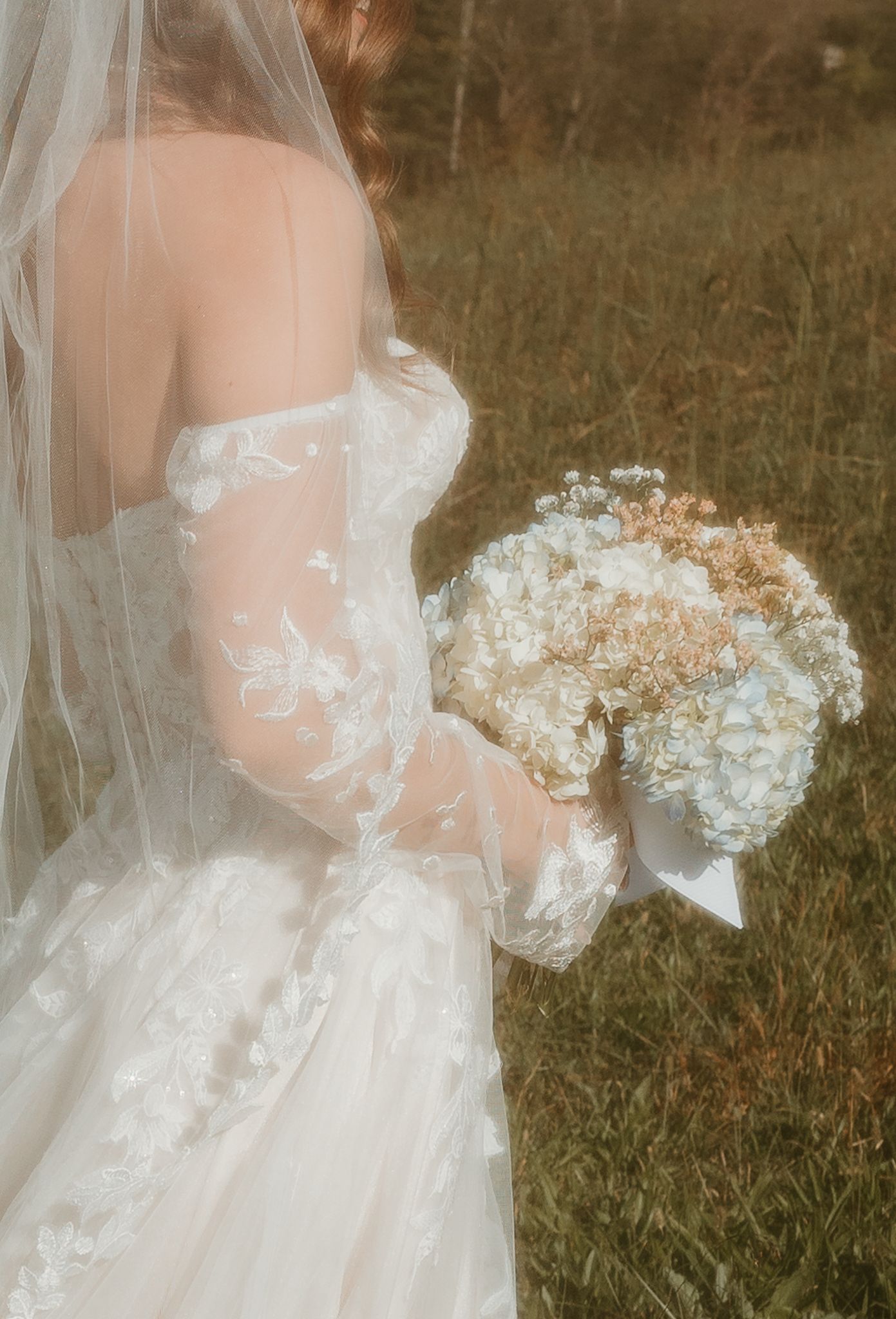 Ethereal bridal portrait showing flowing white wedding dress and bouquet in golden sunlit field.