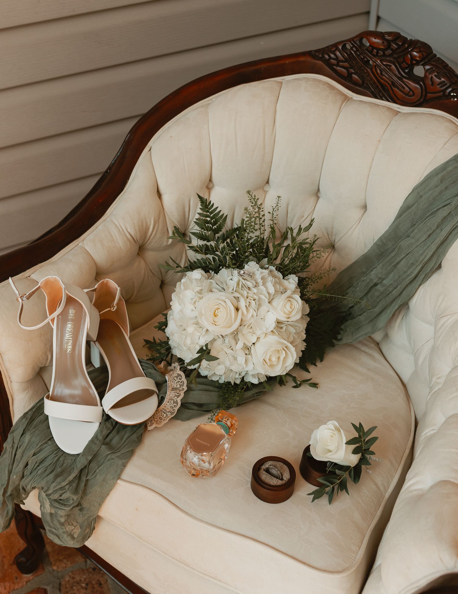 Wedding accessories including white shoes and floral bouquet arranged on cream vintage sofa.