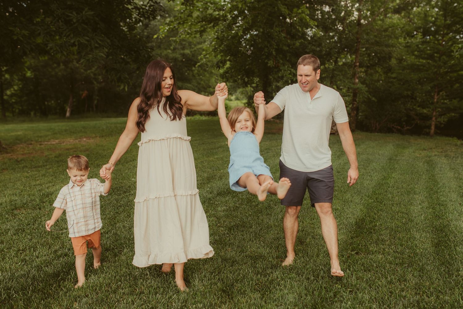 A family walks together holding hands across a green lawn during golden hour. Chattanooga Family Photographer
