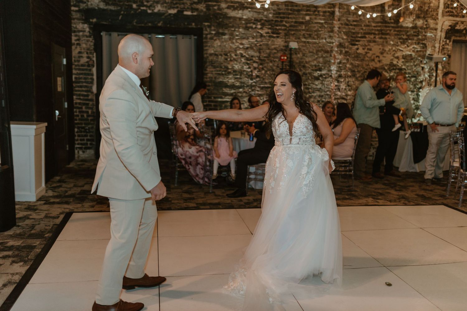 Couple dancing together at wedding reception in rustic brick-walled venue.