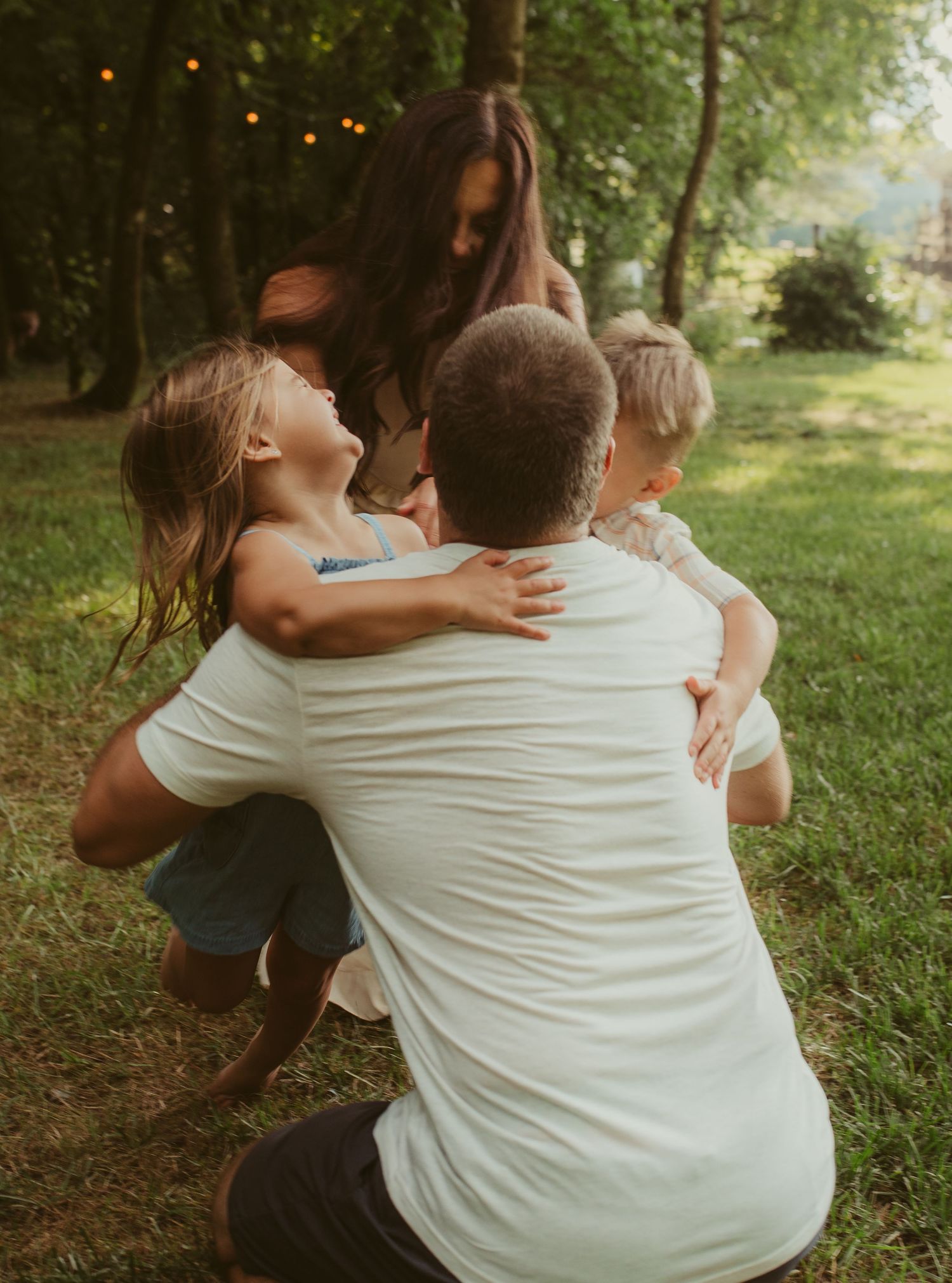 Candid family moments captured in a wooded area with string lights visible in background.