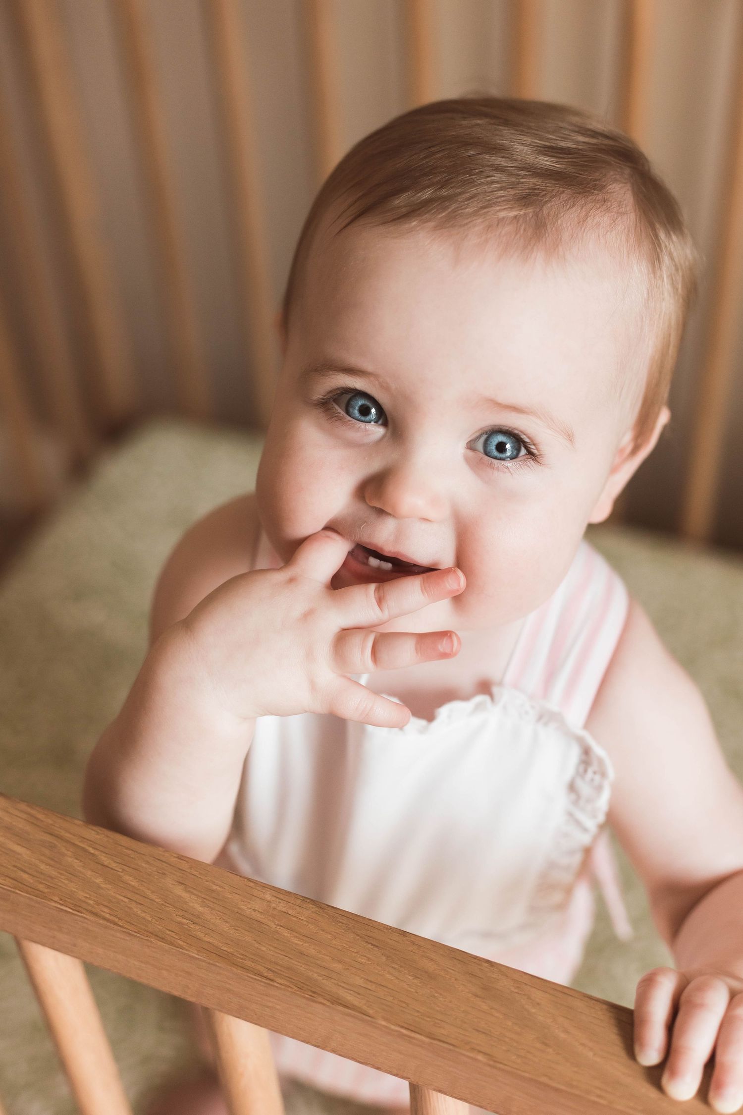 Closeup of a baby with bright blue eyes peeking over wooden crib railing.
