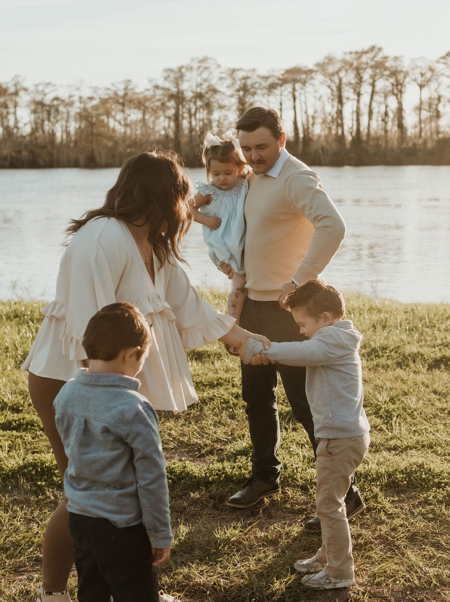 Family plays together on grassy field during golden hour by the water.