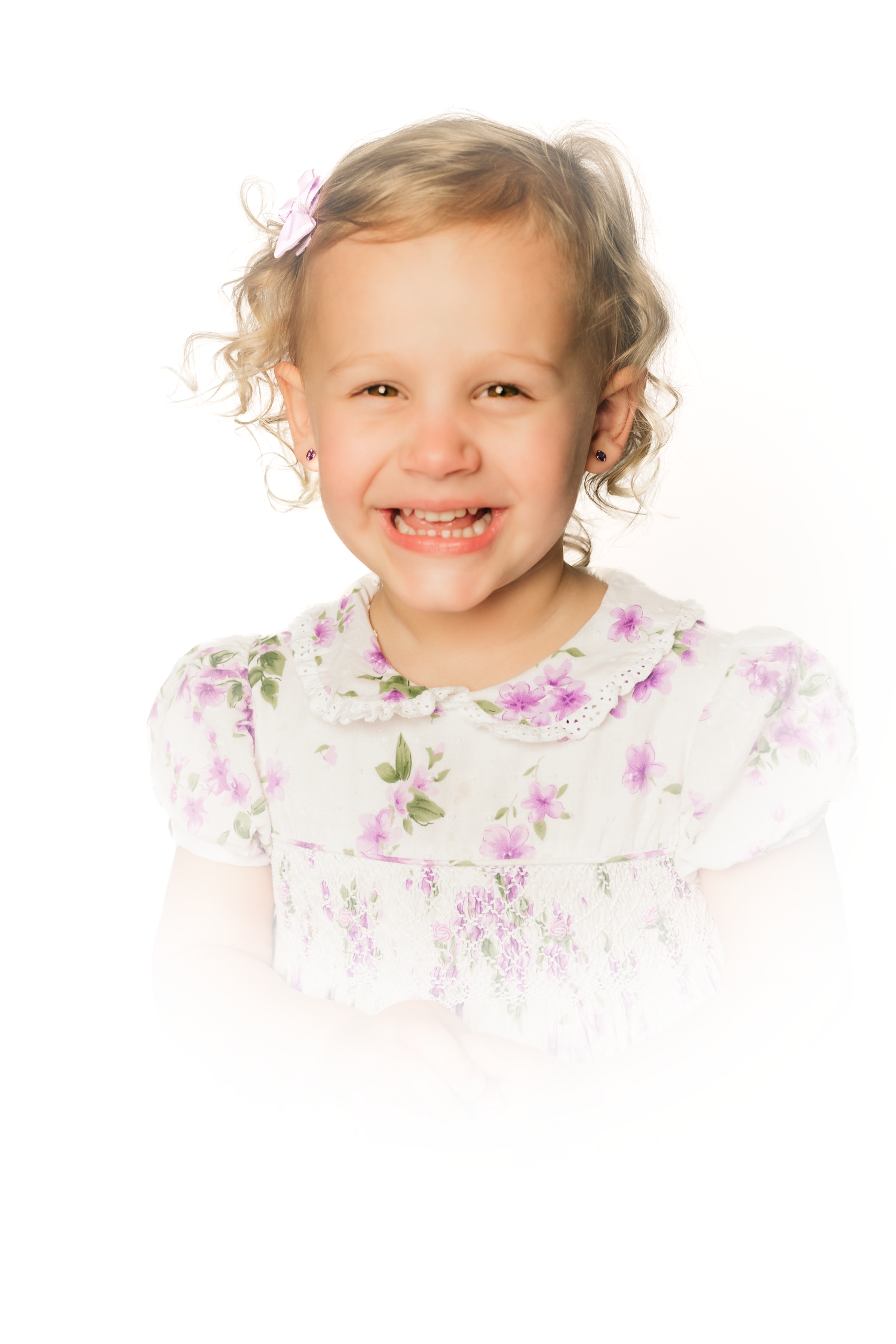 A young child in a floral dress smiling brightly against a white background.