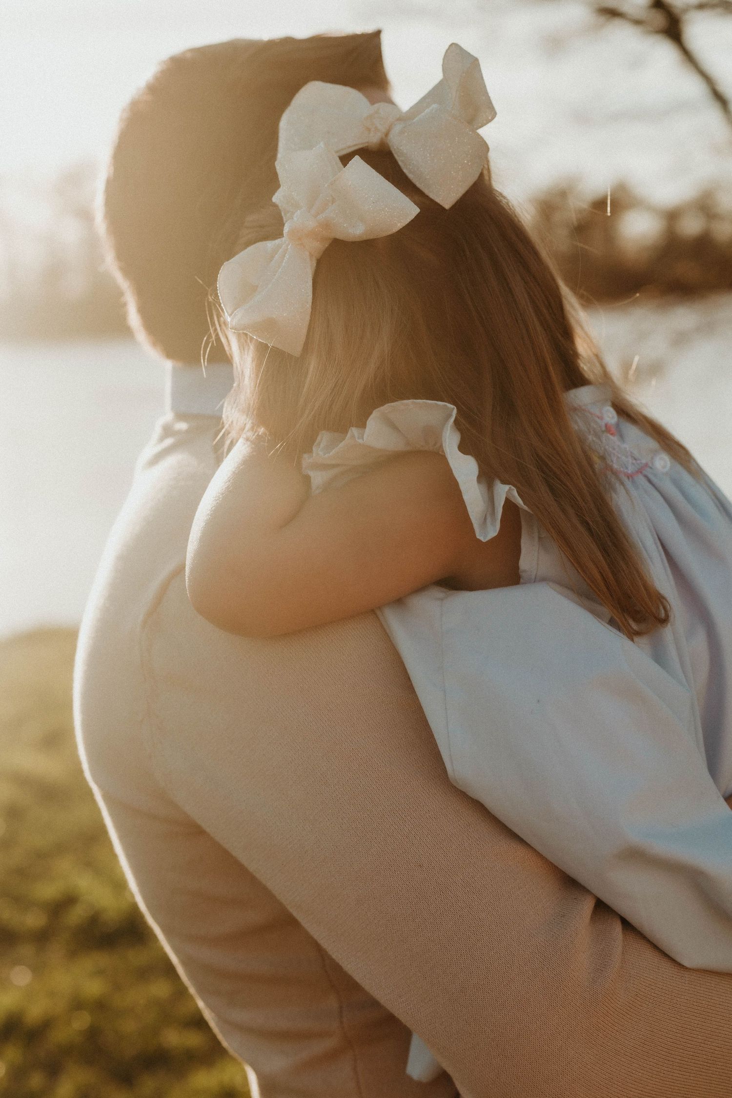 Intimate couple embracing in soft golden sunlight during outdoor photo session.