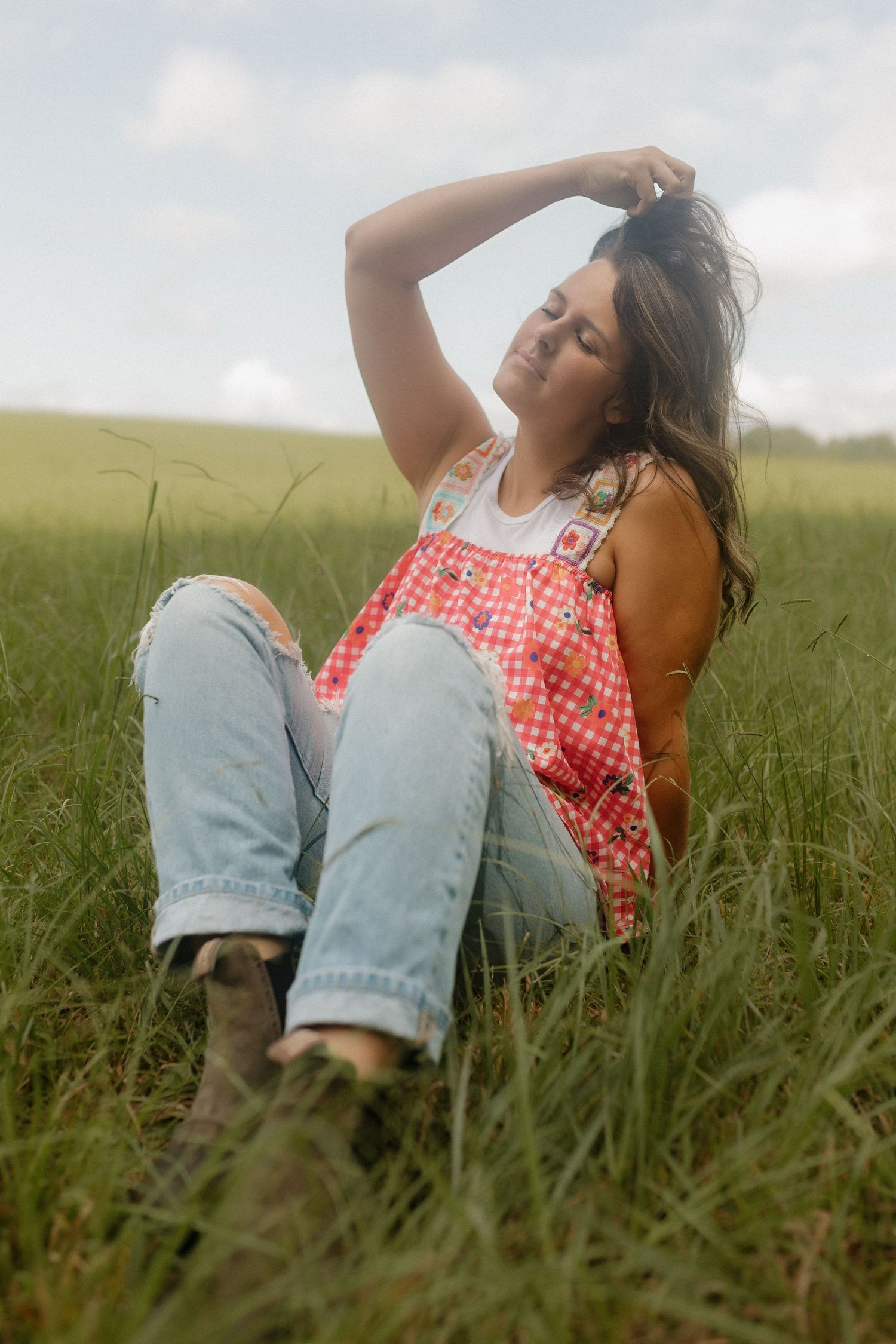 Someone relaxing in a grassy field wearing distressed jeans and a red patterned top on a sunny day.