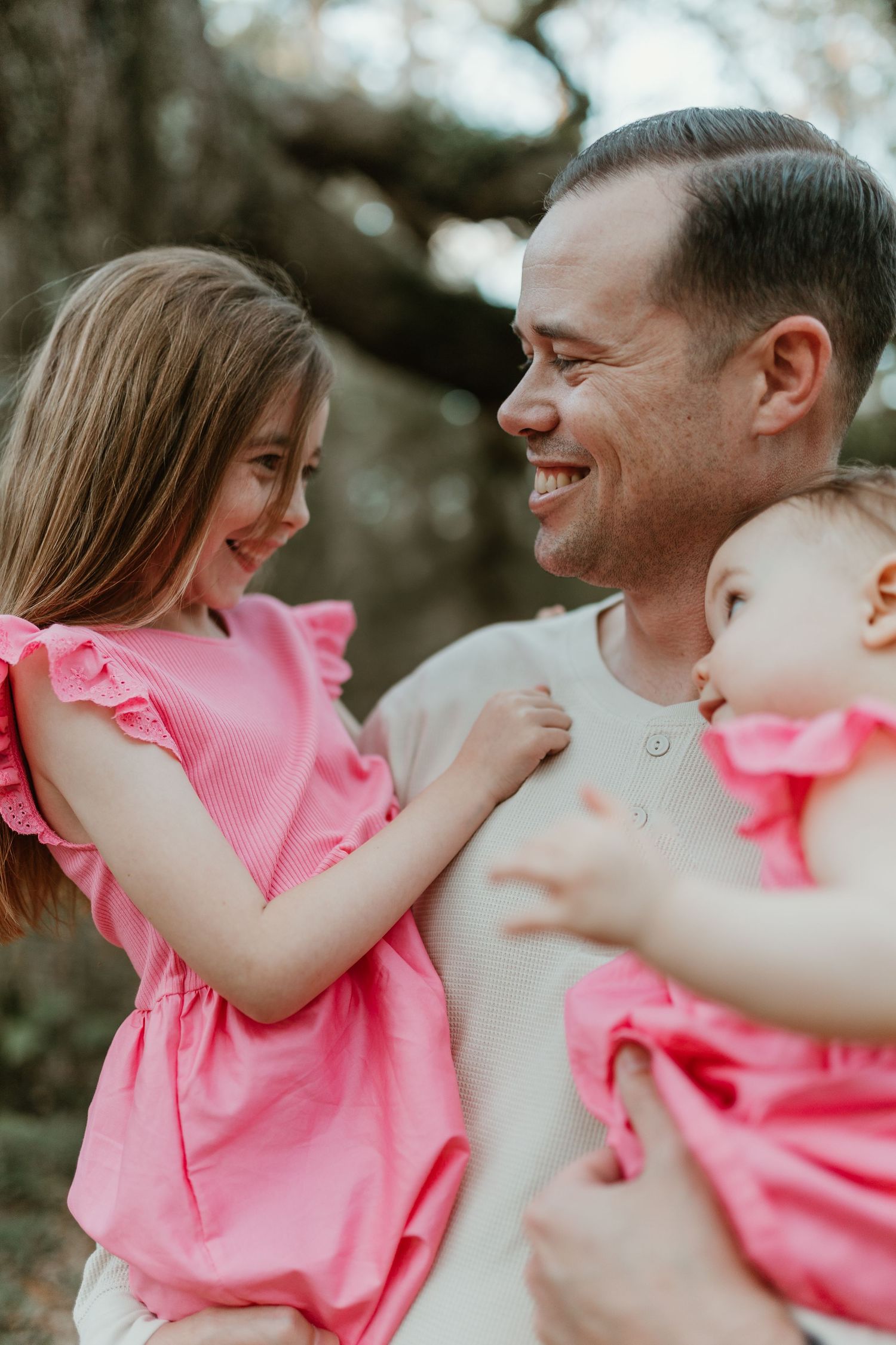 A joyful outdoor family moment with matching pink outfits against a natural forest backdrop.