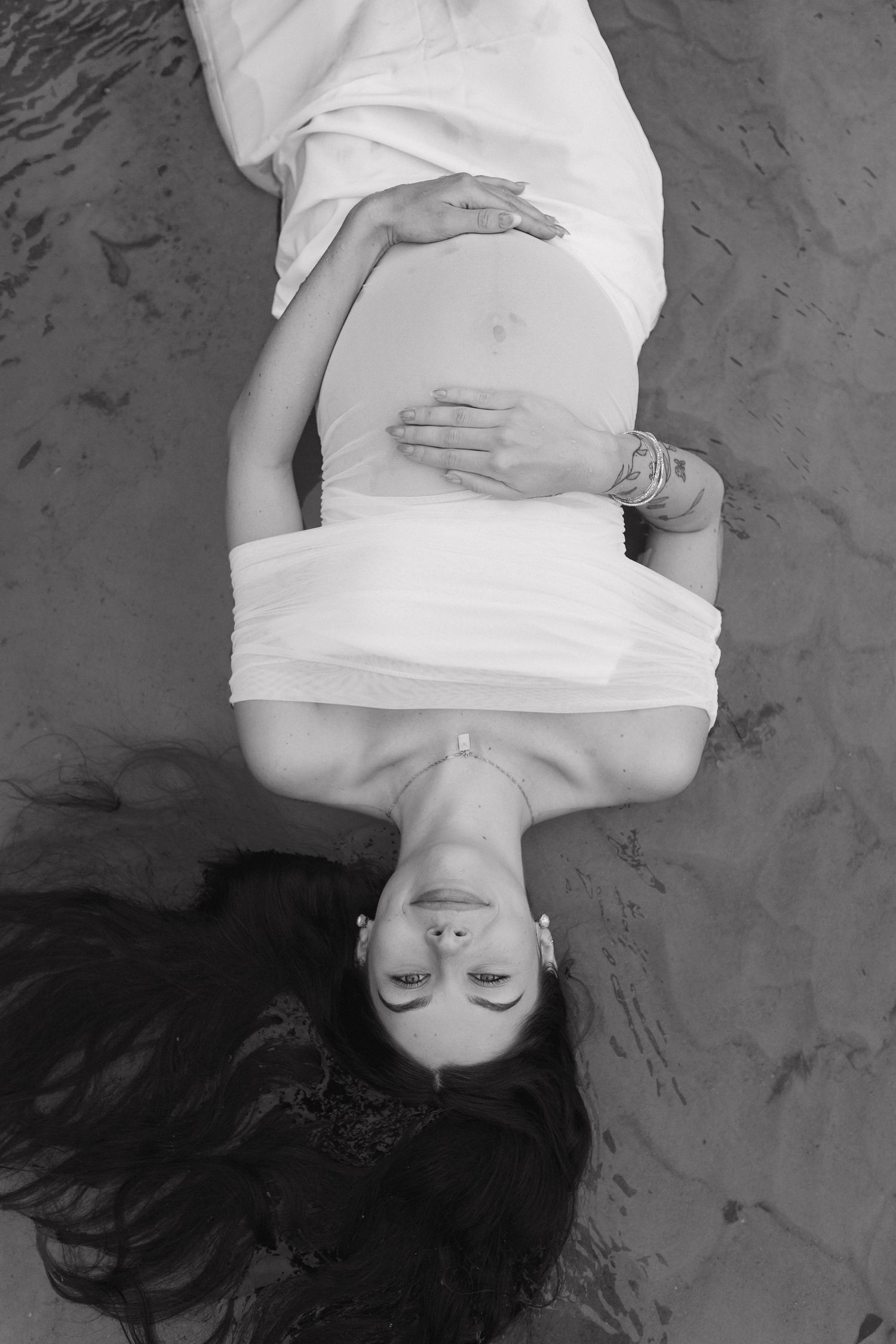 Black and white artistic maternity photos showing a woman lying down in a white dress.