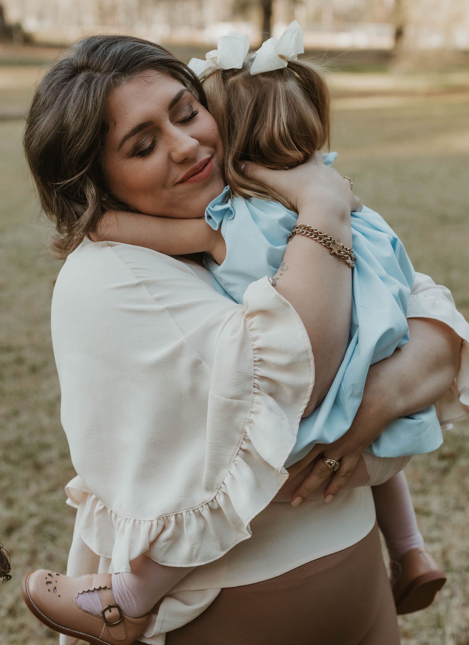 Mother in white ruffled top embraces children in outdoor portrait series.