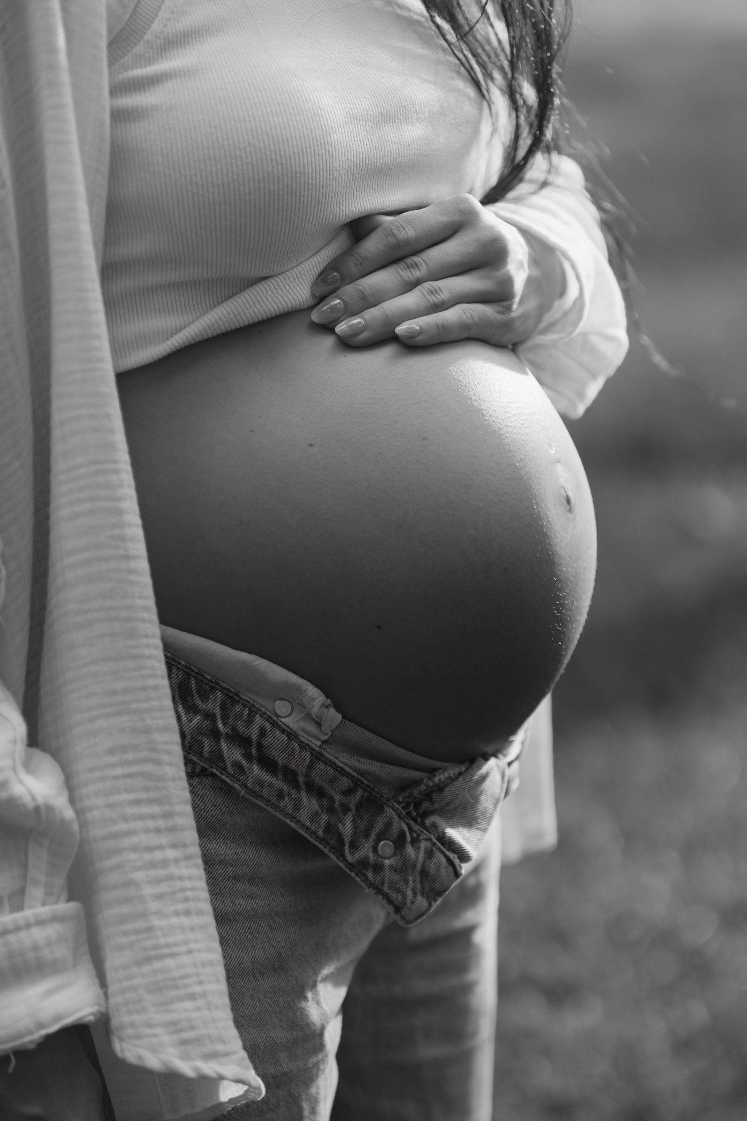 Close-up black and white photo of pregnant belly with hands gently resting on top.