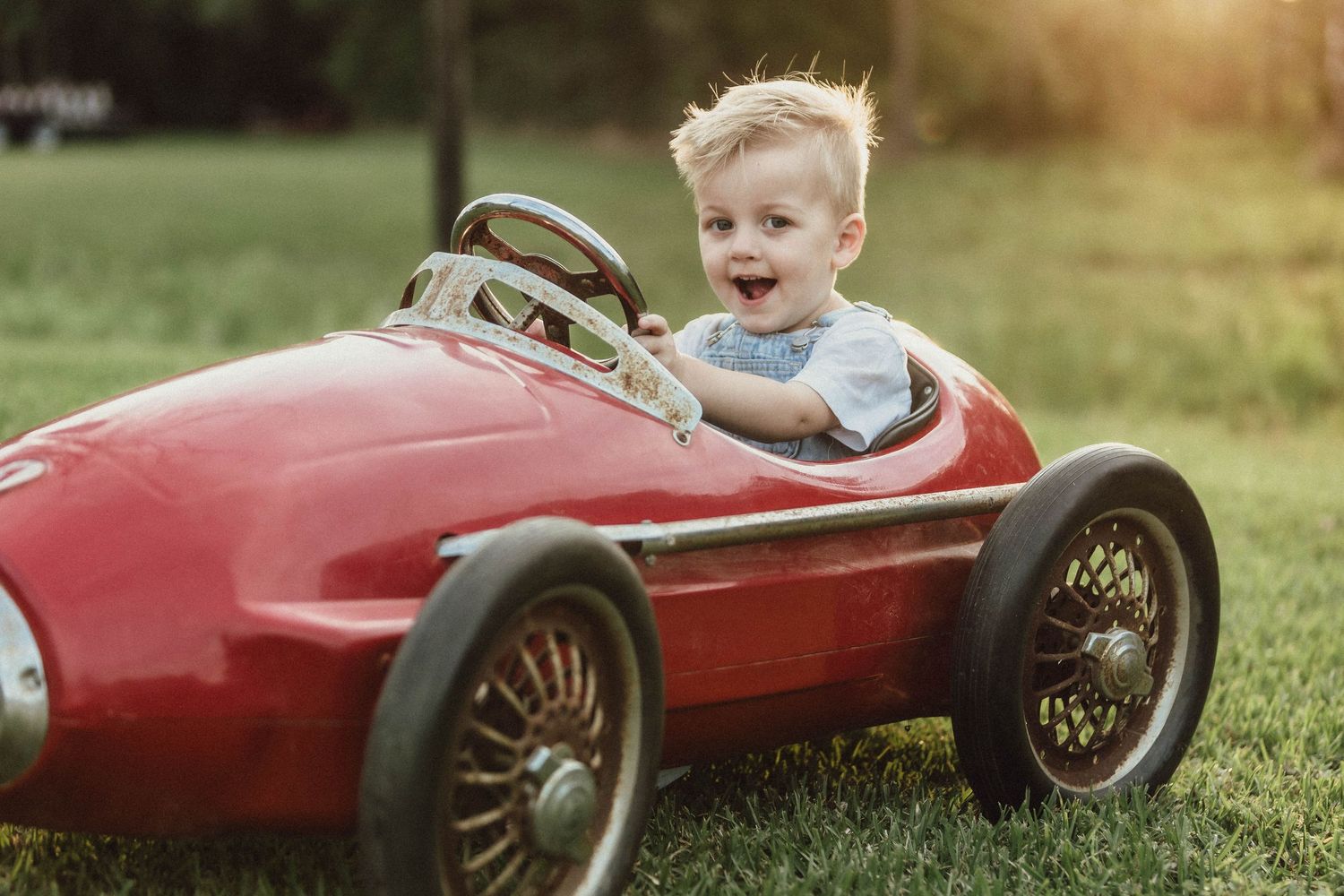Vintage red toy racing car photographed in field during golden hour.