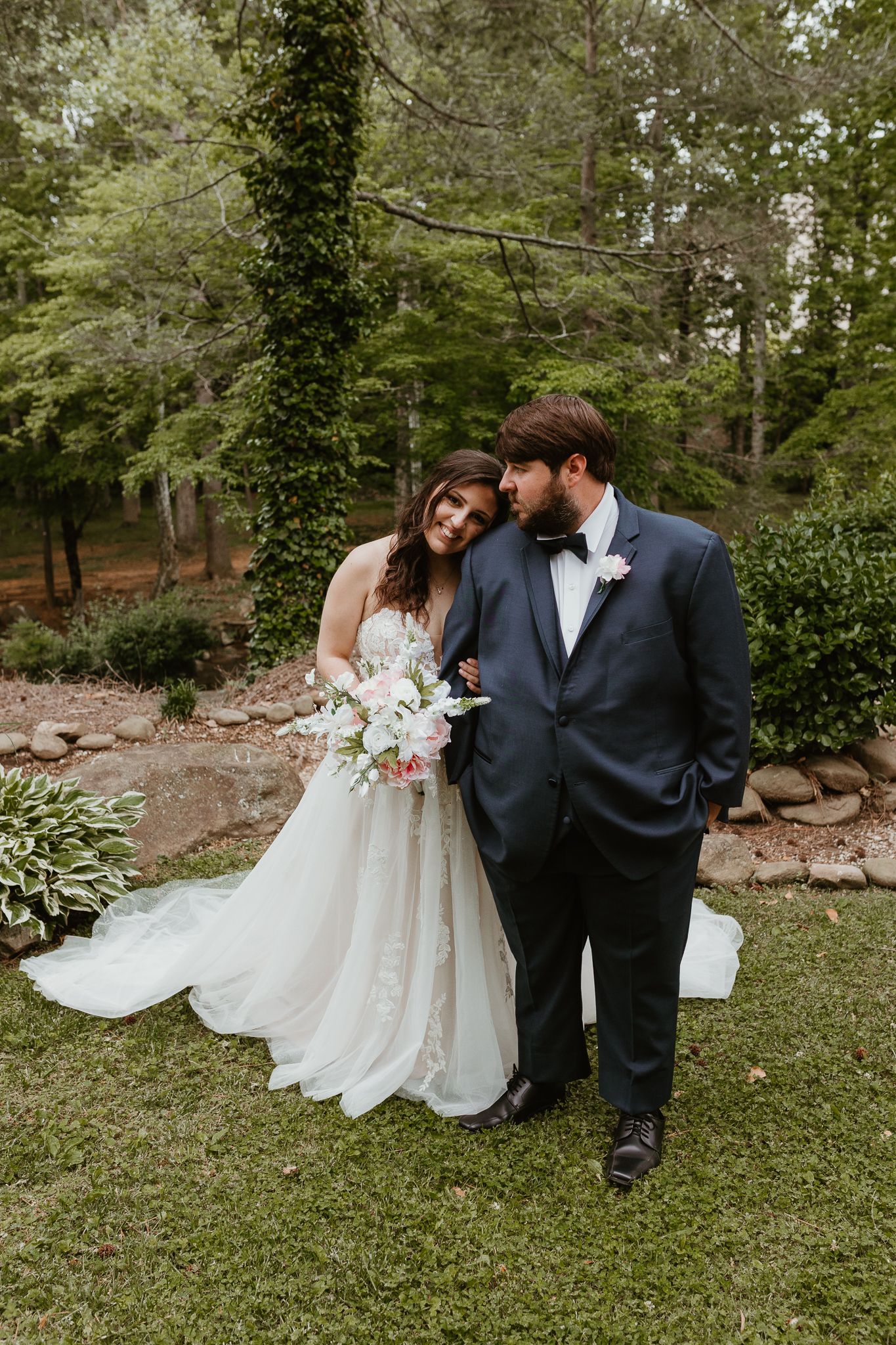Newlywed couple sits together on lush grass during outdoor wedding photoshoot.