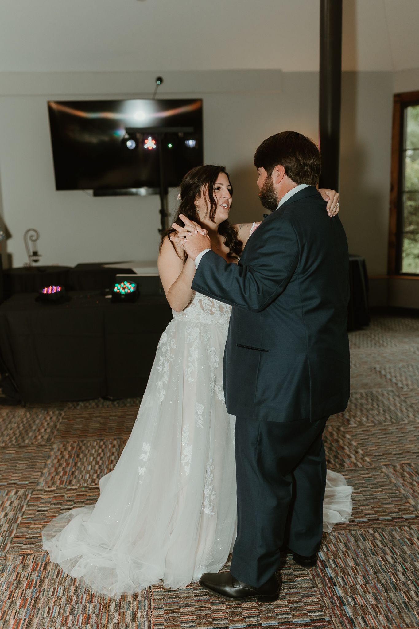 Wedding couple shares first dance in elegant indoor venue with patterned floor.