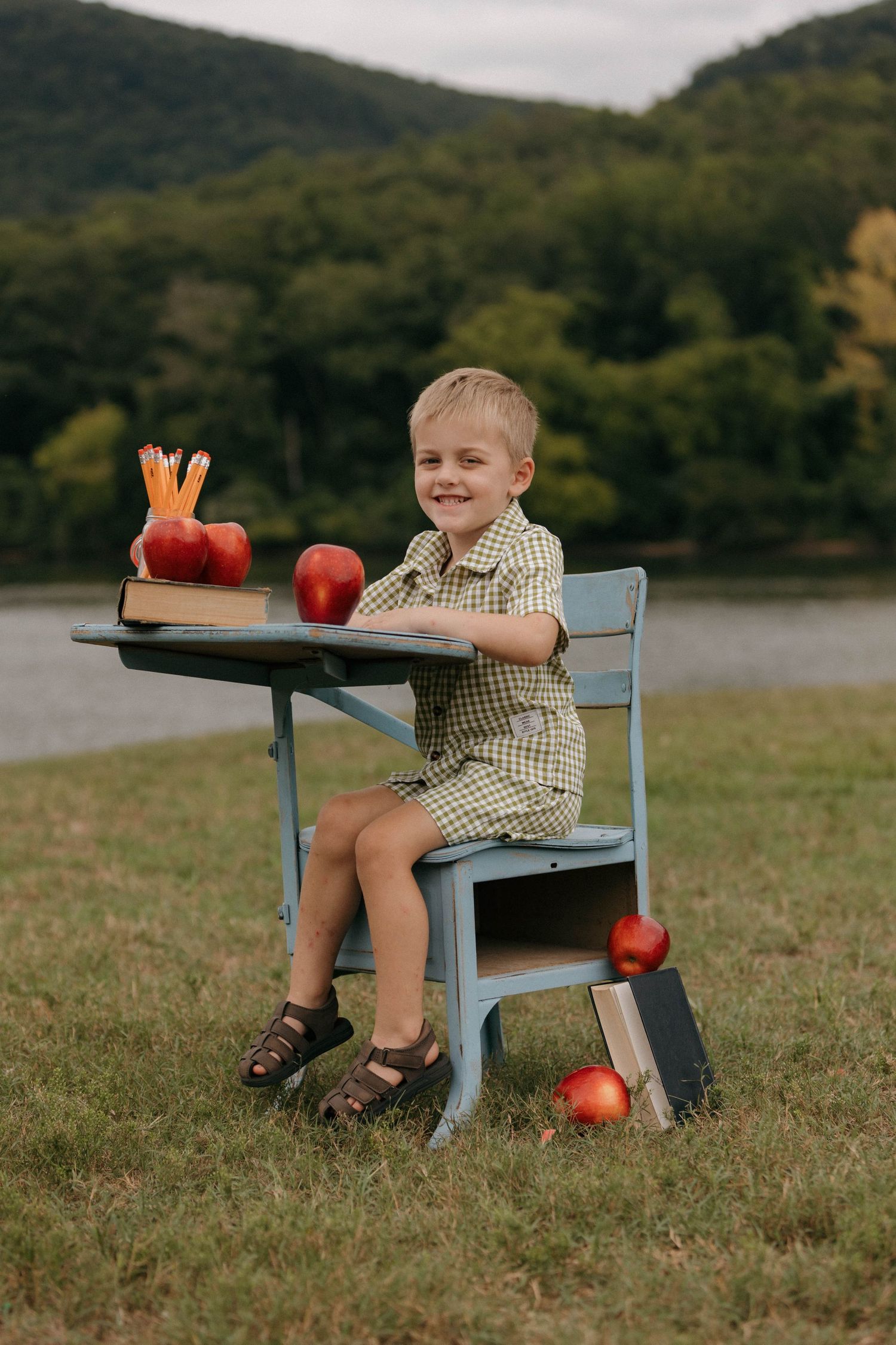 Child sitting at blue vintage desk with red apples in outdoor setting.