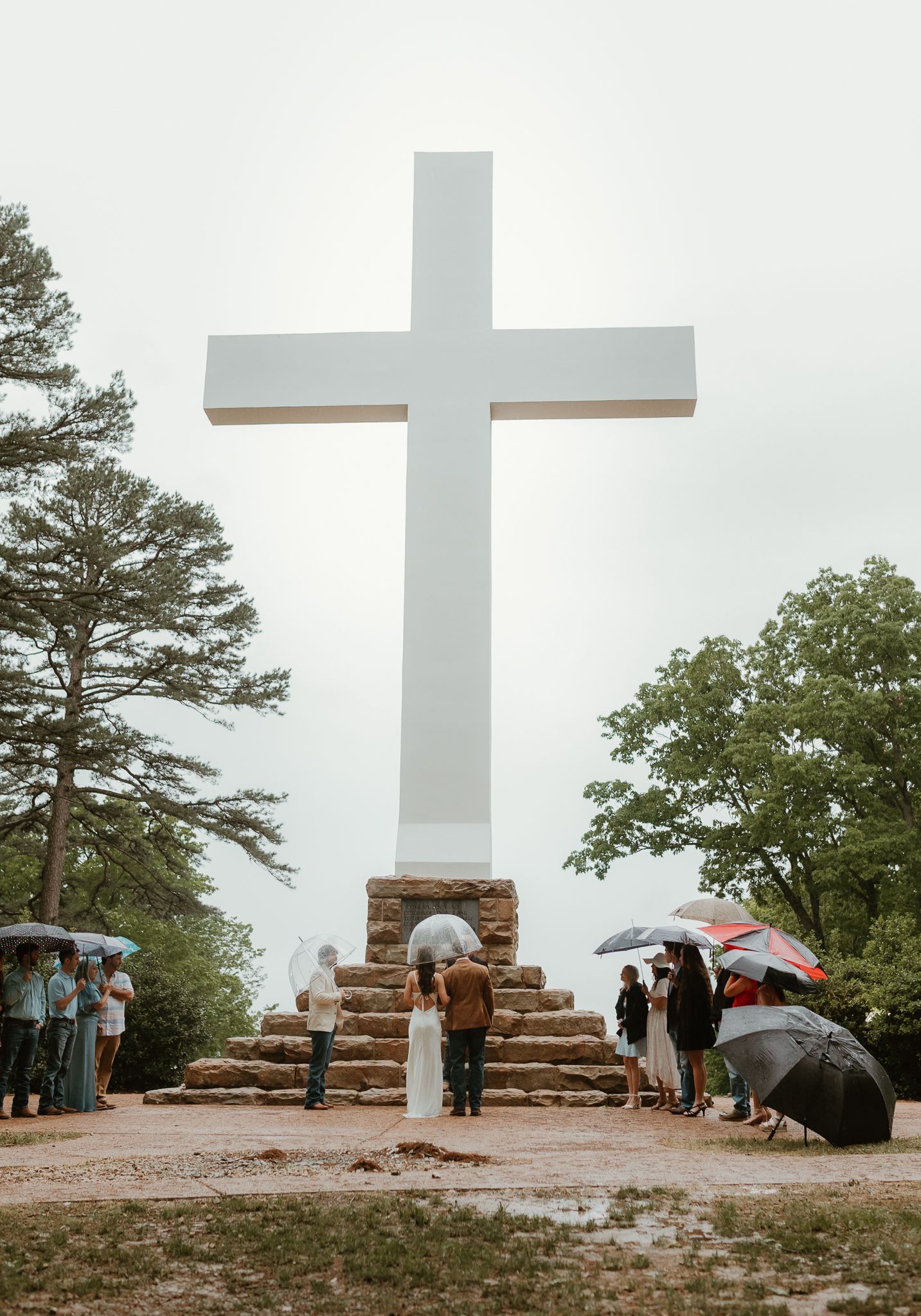 Dramatic white cross monument overlooks scenic landscape with scattered guests.
