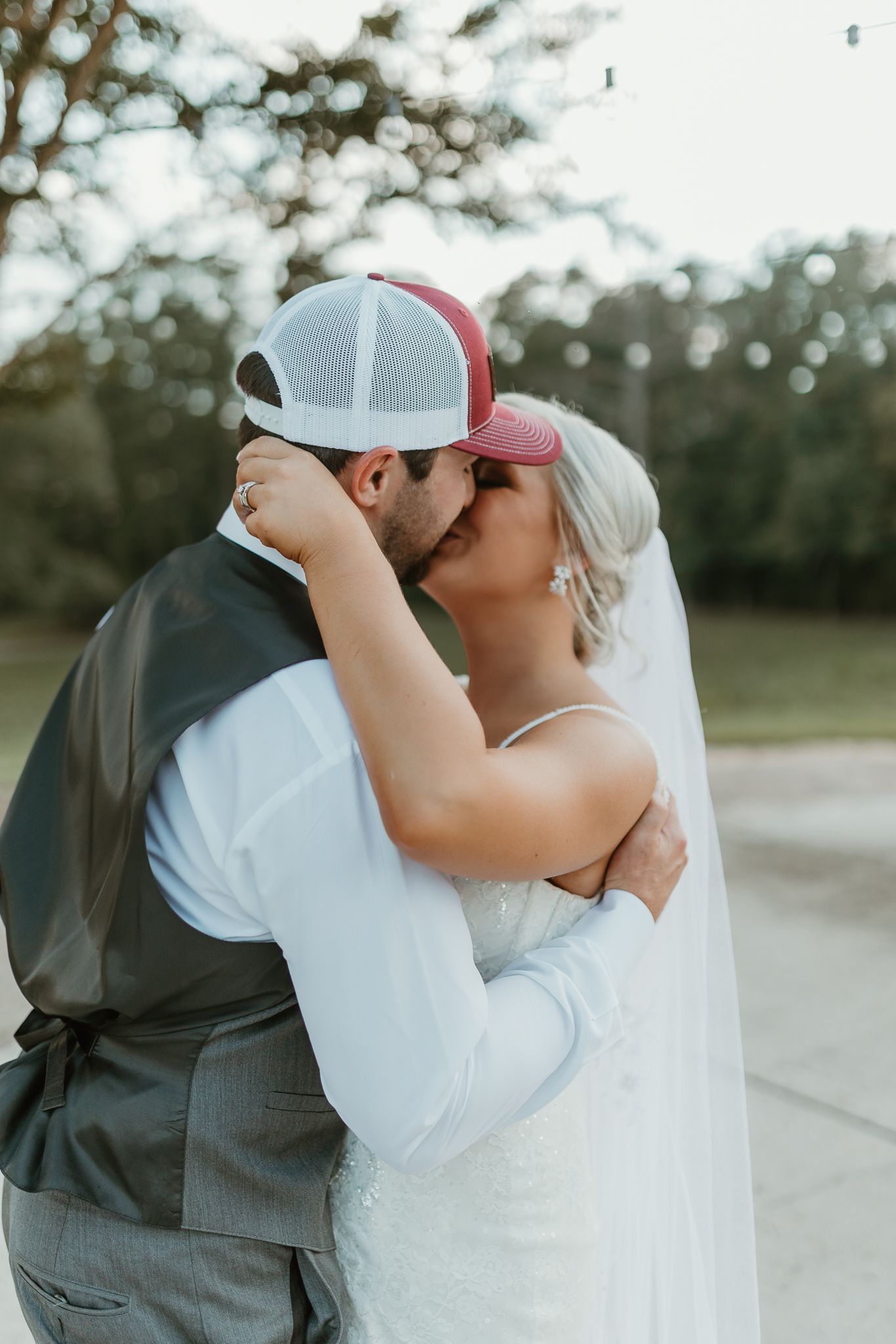 A tender wedding moment captured as newlyweds embrace and kiss in an outdoor setting.