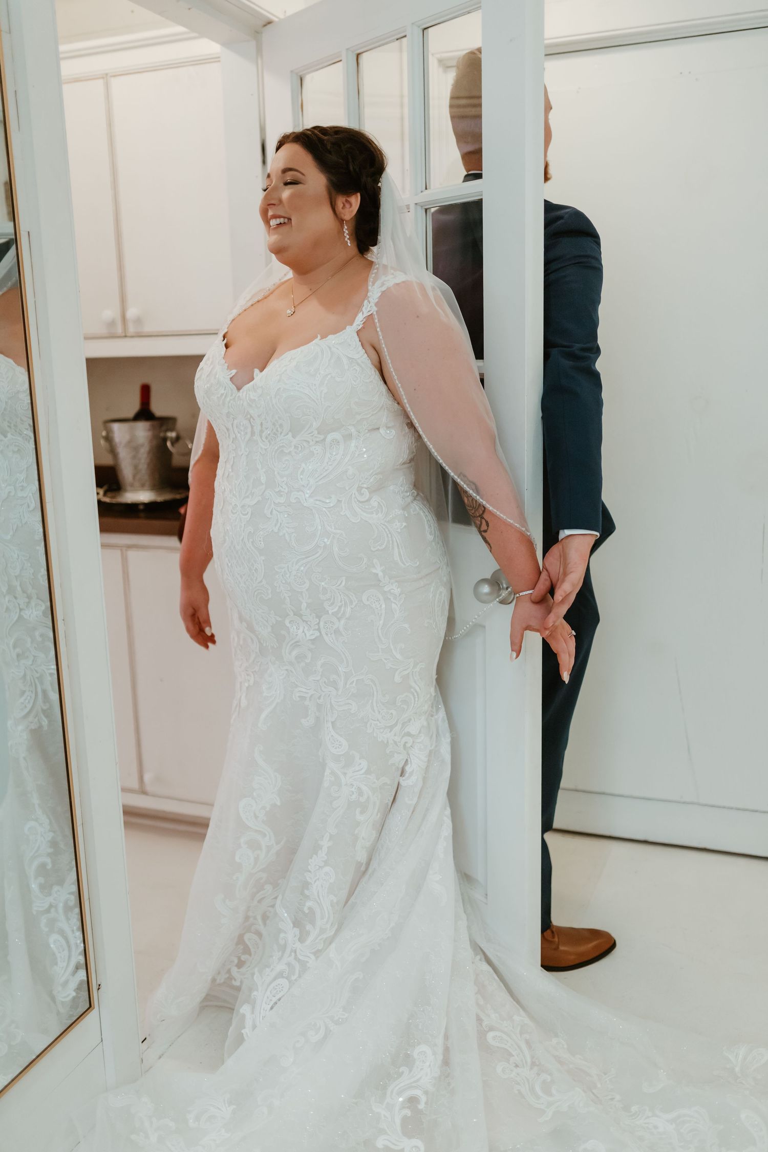 A beautiful lace wedding dress being fitted in a bridal boutique with mirrors.