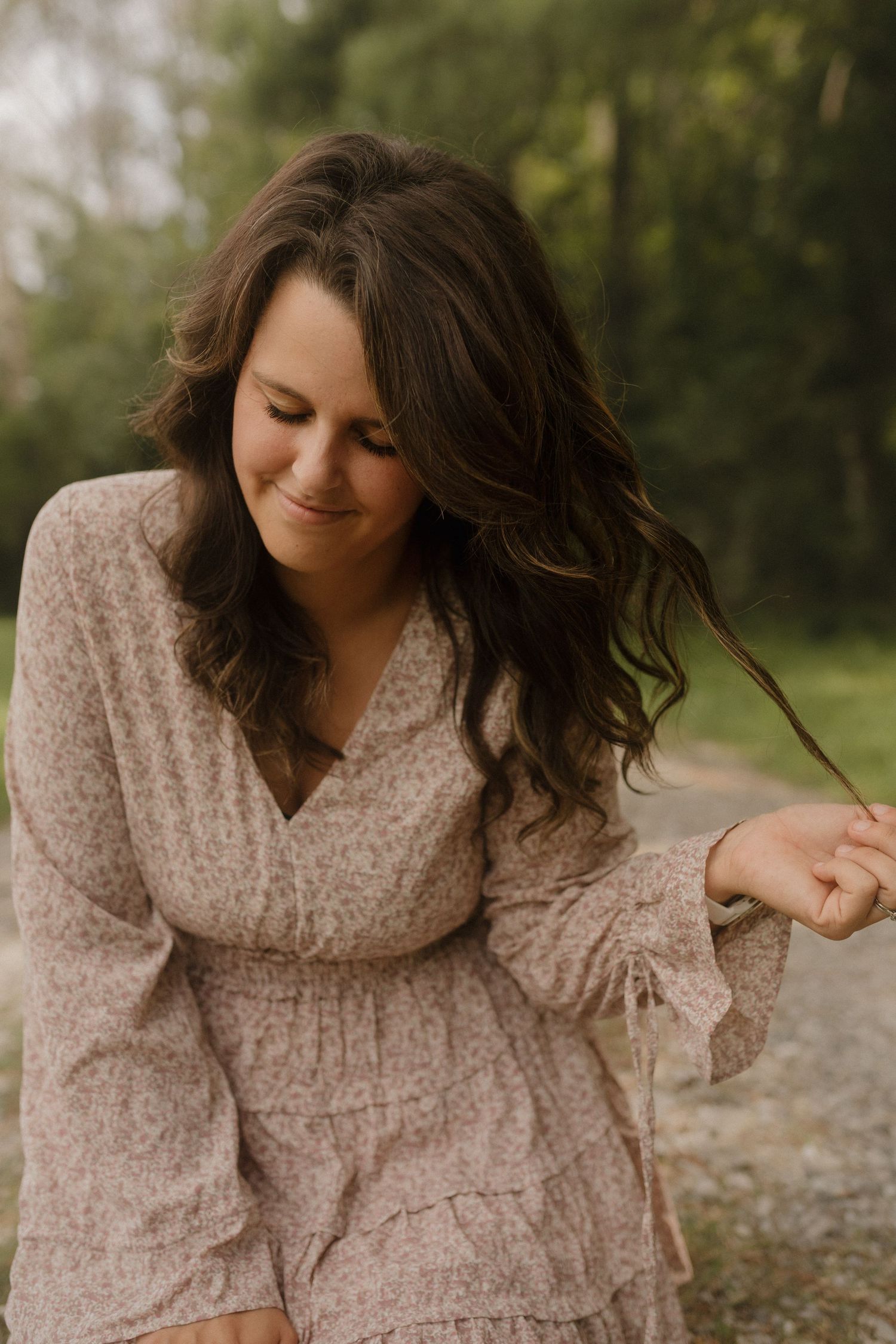 Someone in a beige textured dress poses playfully on a path surrounded by trees.