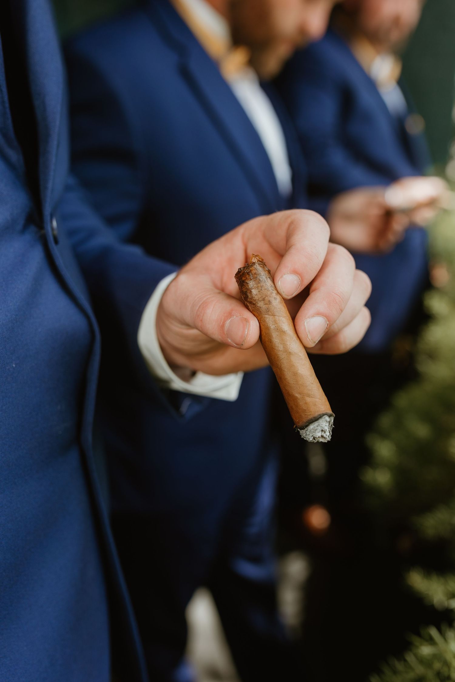 Groomsmen in navy suits lighting cigars during wedding celebration.