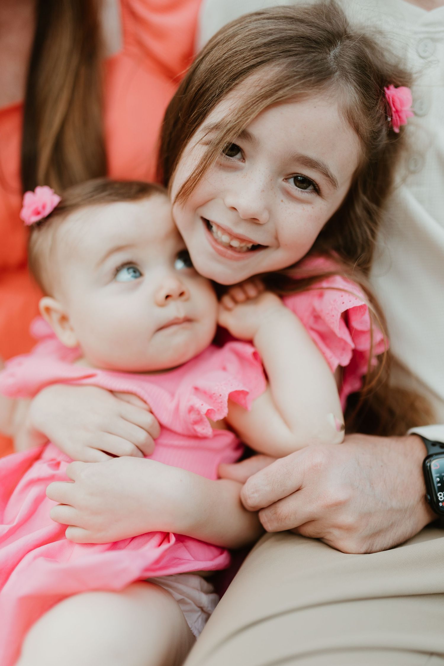 Two children in pink outfits share a sweet sisterly moment during a family photo session.