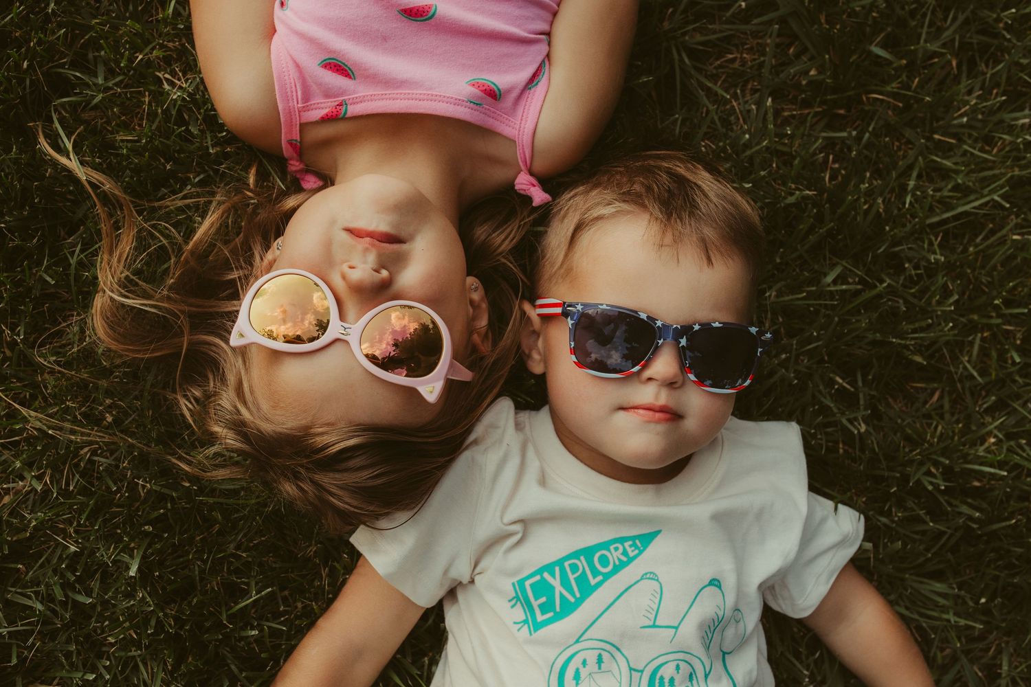 Children laying in grass wearing sunglasses during a fun summer photoshoot.