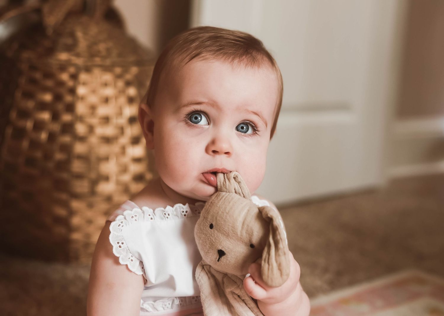 Baby in white lace dress with bright blue eyes looking at camera.