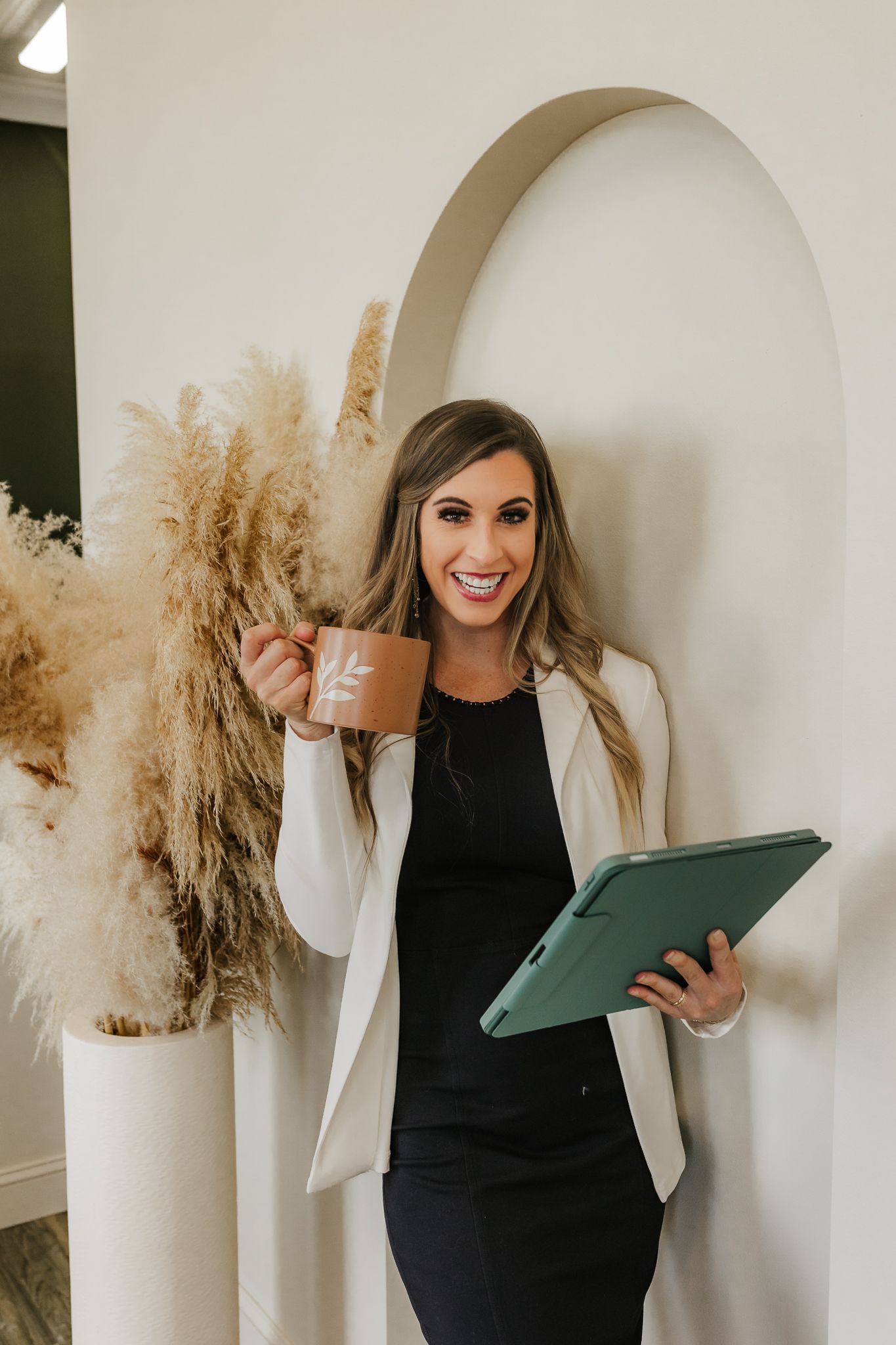 Professional headshots with white blazer and portfolio against neutral backdrop with pampas grass.