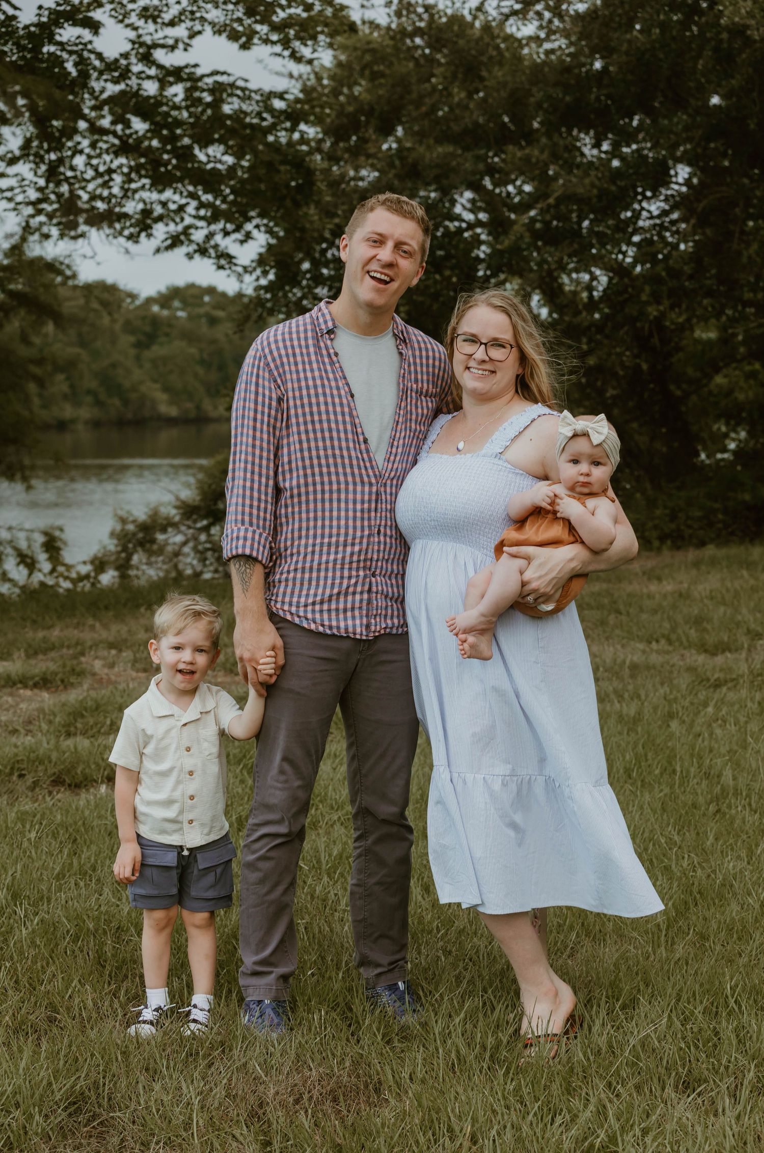 A casual family portrait by the lake with everyone dressed in coordinated outfits.