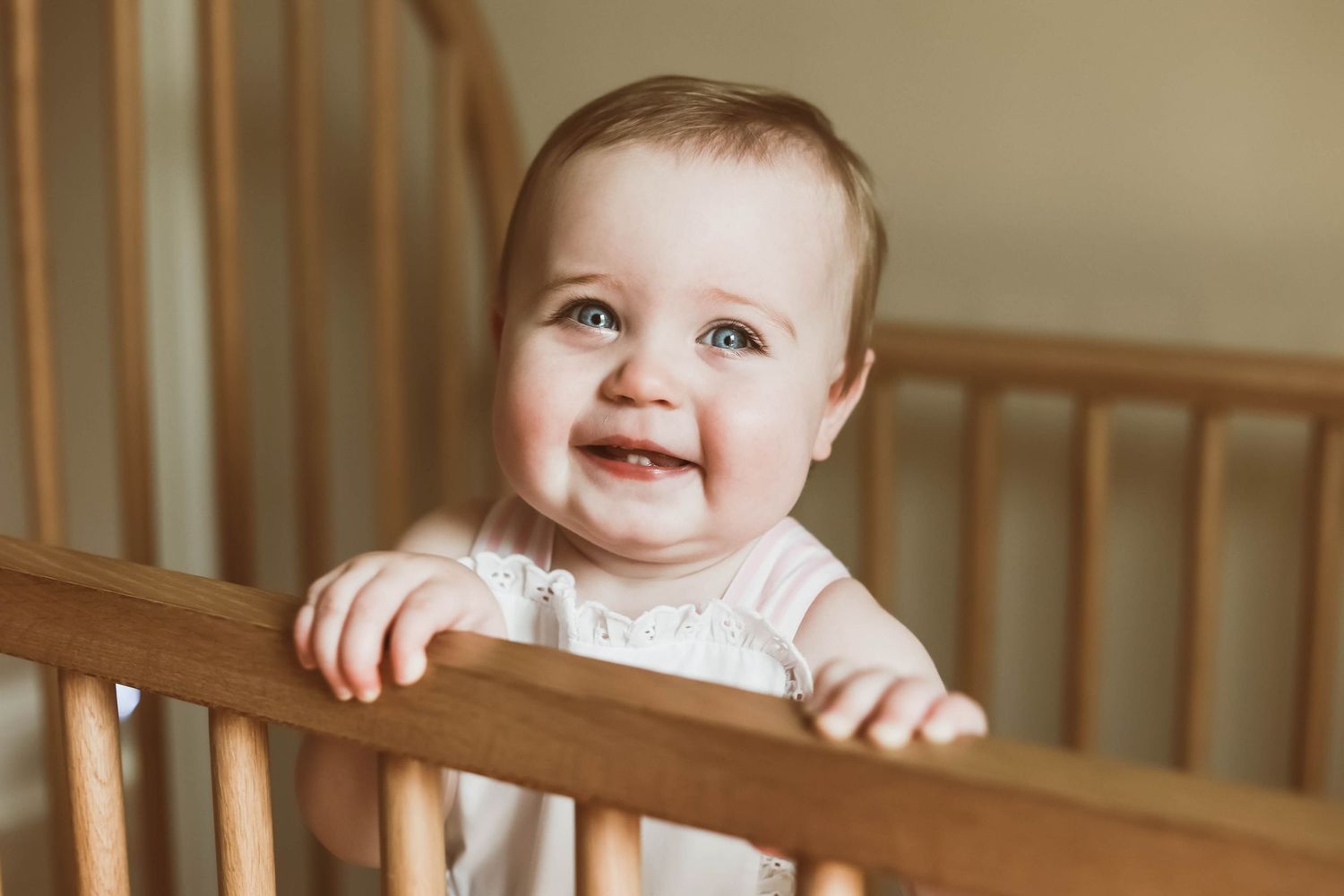 Baby in a wooden crib smiles while holding onto the railing.