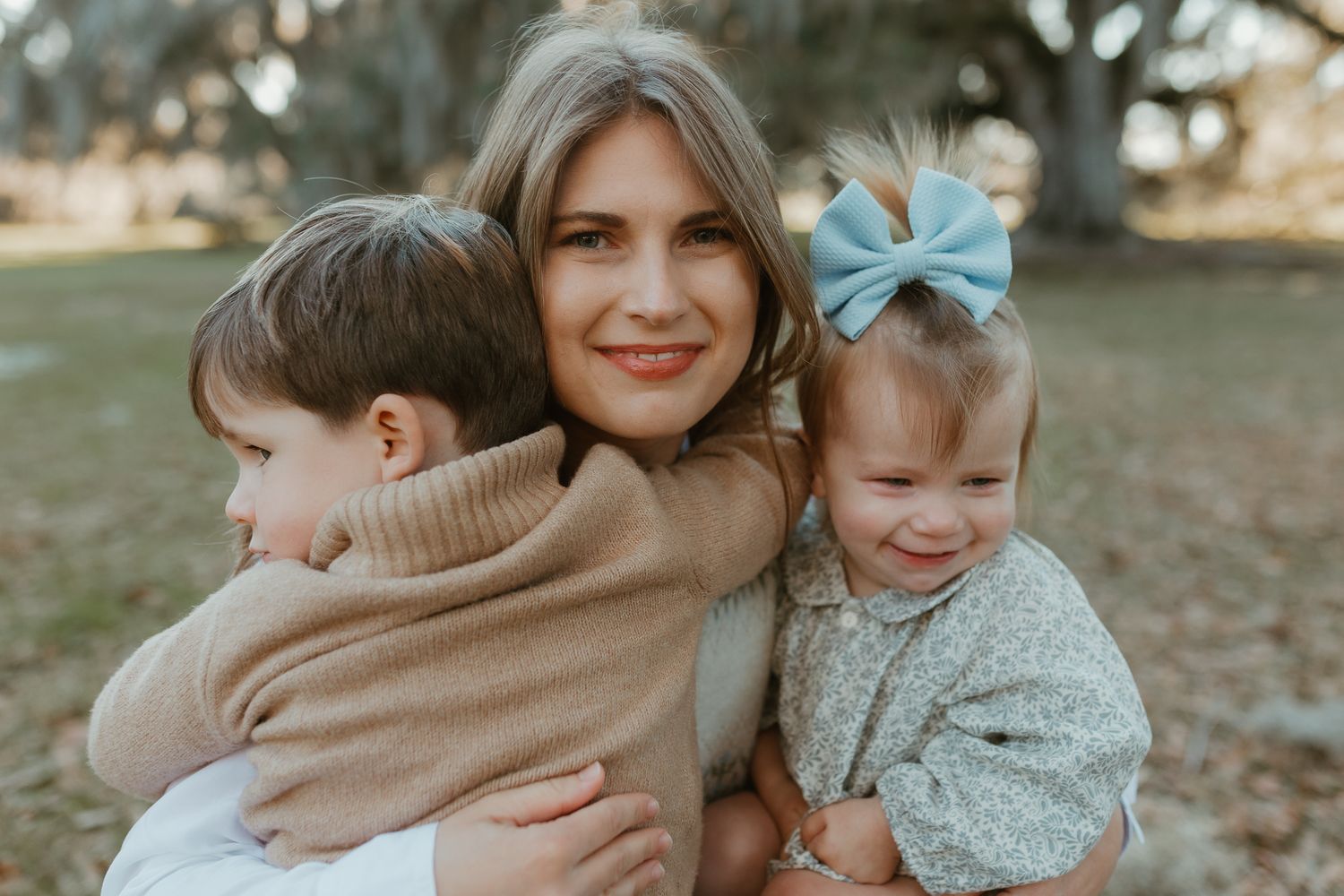 A warm outdoor family portrait showing tender embraces and joyful smiles in a natural setting.