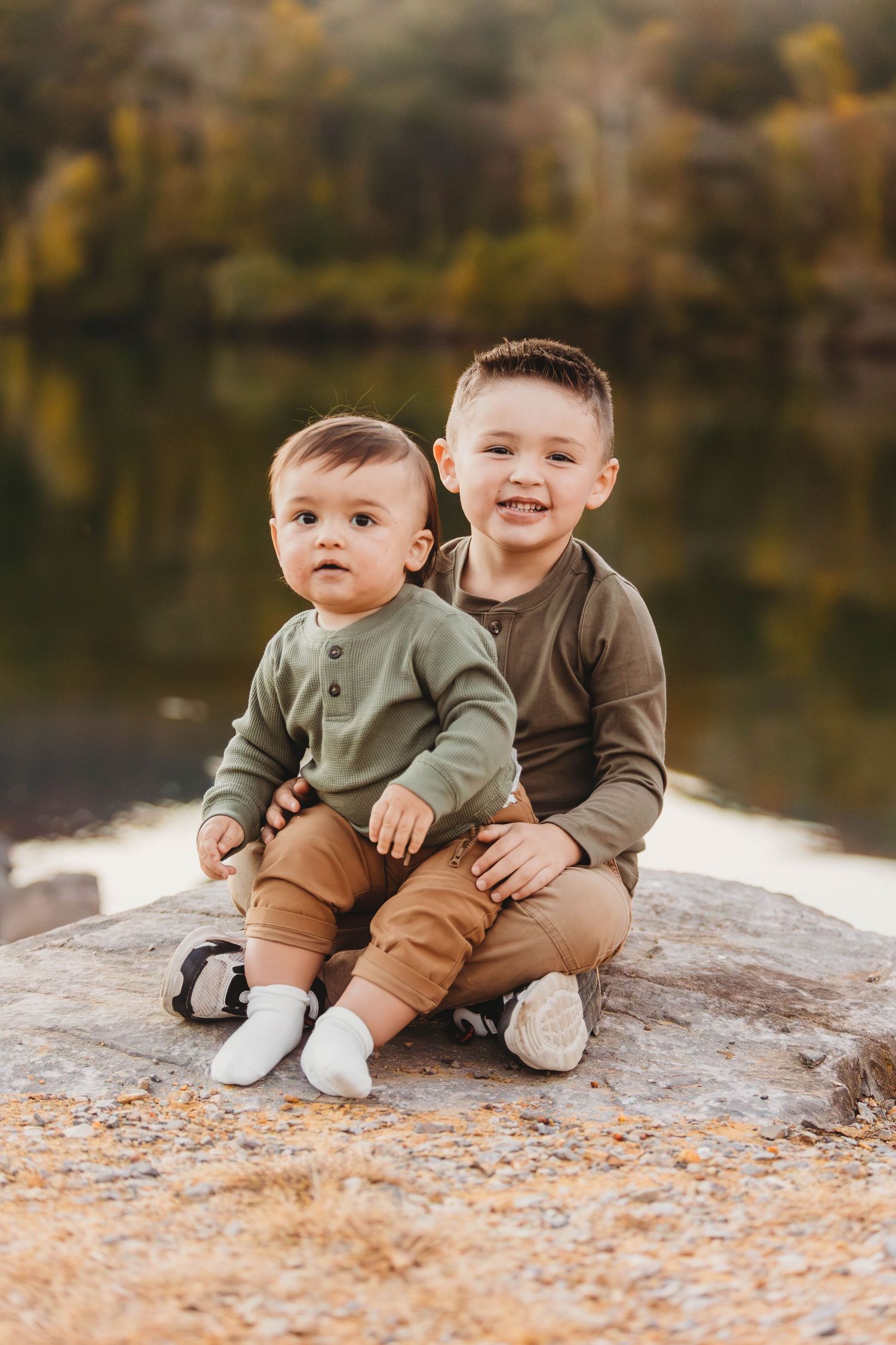 Two children in coordinating outfits sitting together on a rock by a lake in autumn Chattanooga Family Photographer