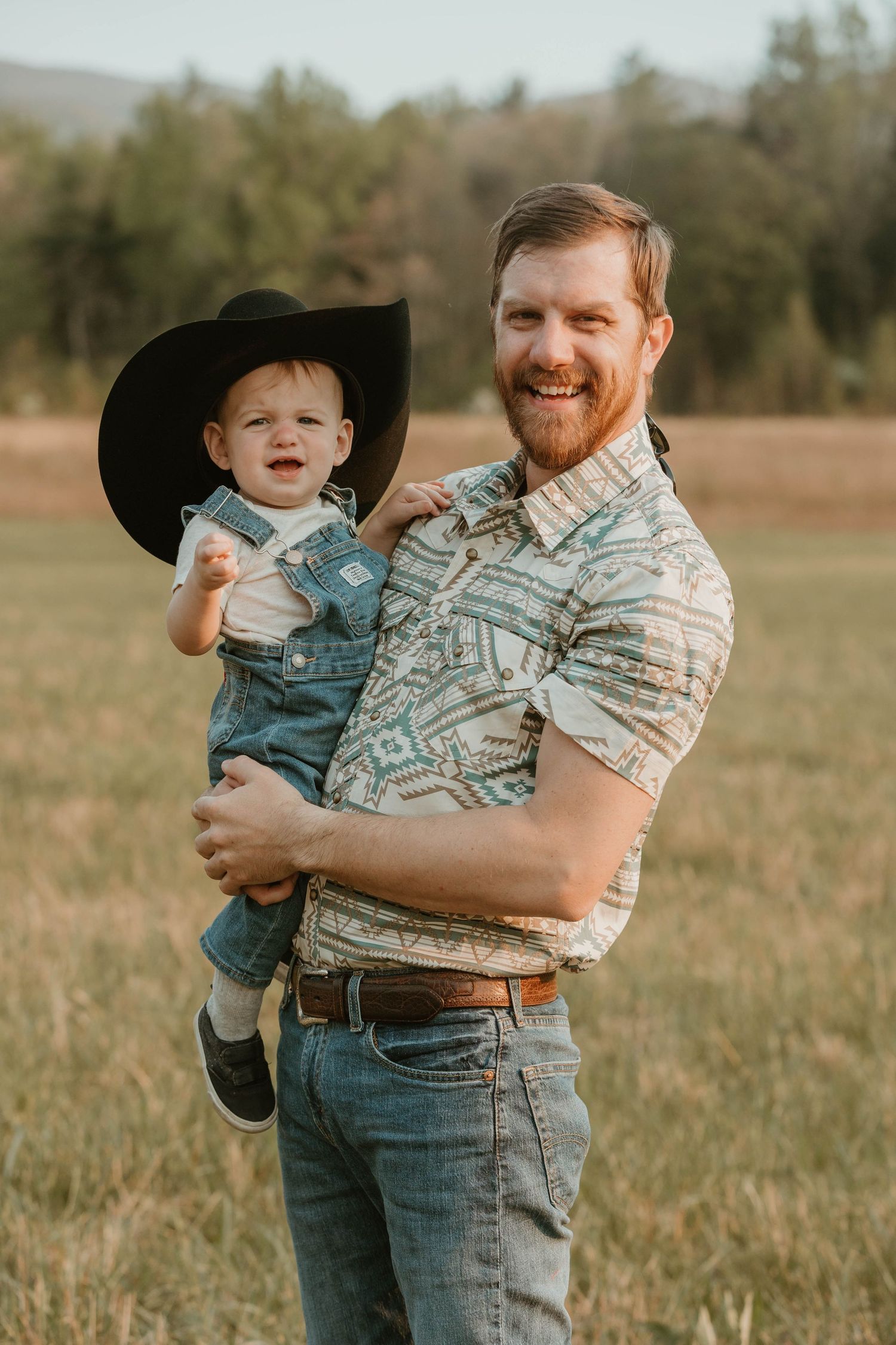 A western-themed photo shoot in a field with cowboy hat and casual attire.