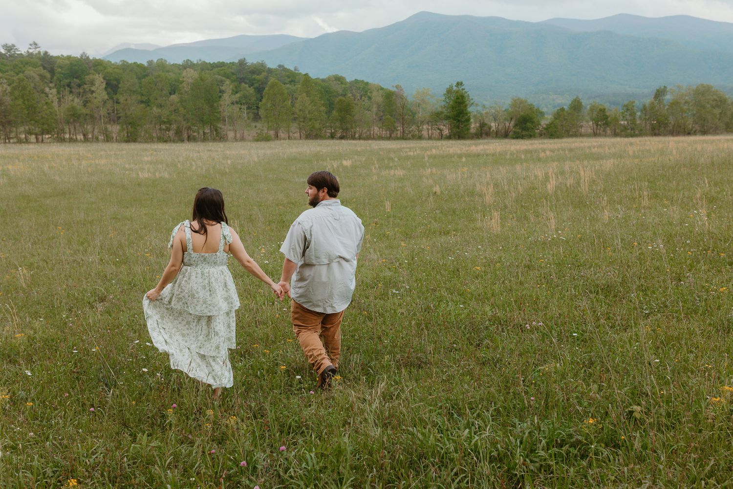 Couple walking hand in hand through a mountain meadow at sunset.
