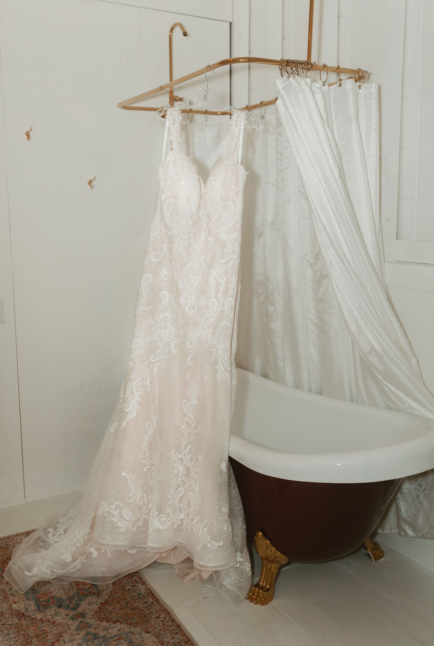 White lace wedding dresses hanging in a room with a vintage clawfoot bathtub.
