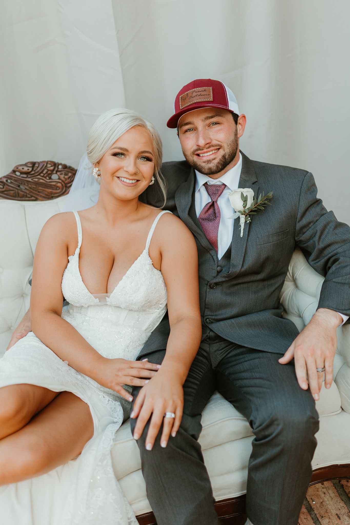 Wedding couple sitting close together on a white couch in casual and formal attire.