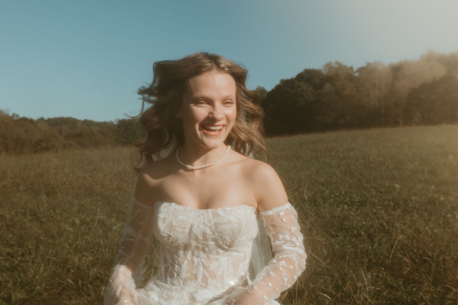 Elegant off-shoulder lace wedding gown captured in warm outdoor lighting.