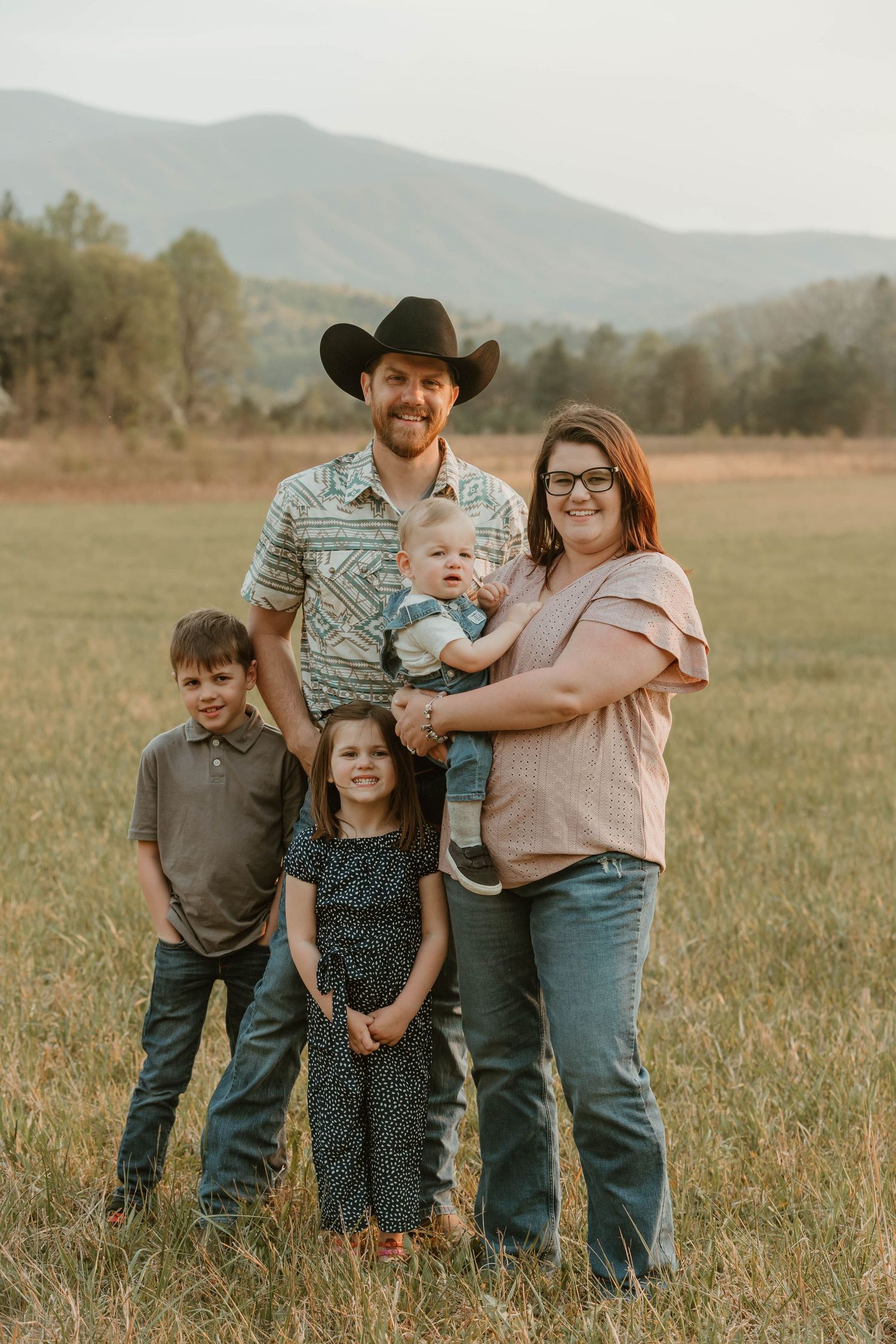 Family portrait in a rustic field with mountains visible in the background.