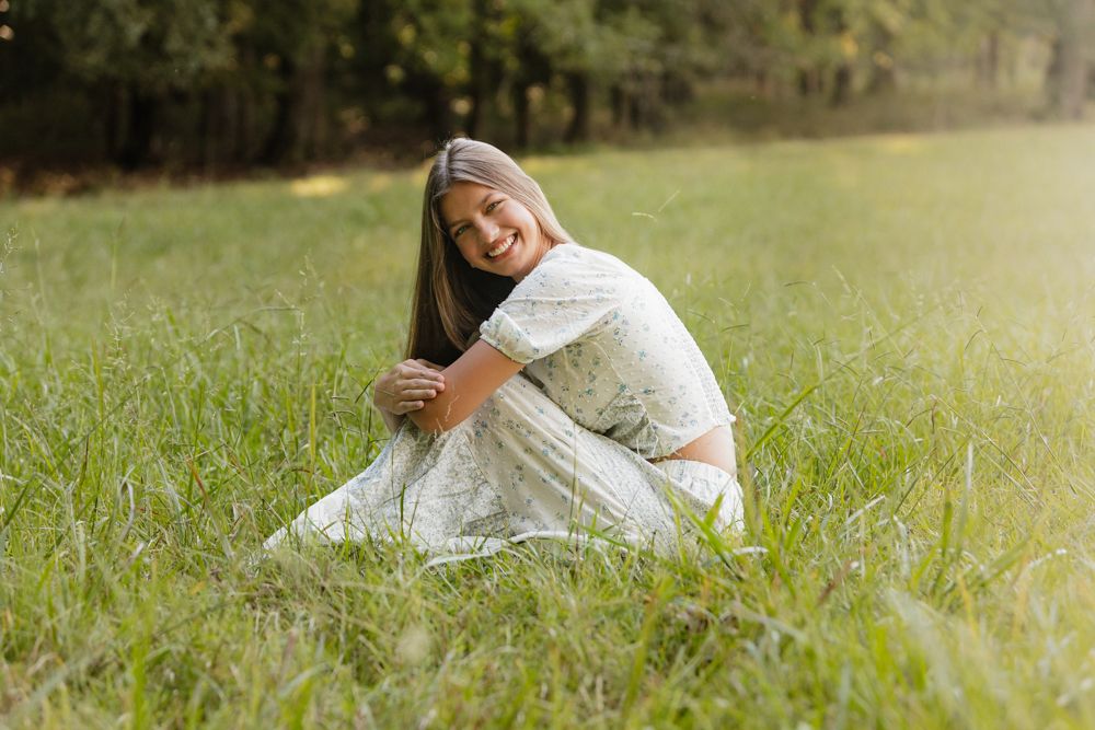 A person in a white dress lies peacefully in a sunlit grassy meadow on a warm summer day.