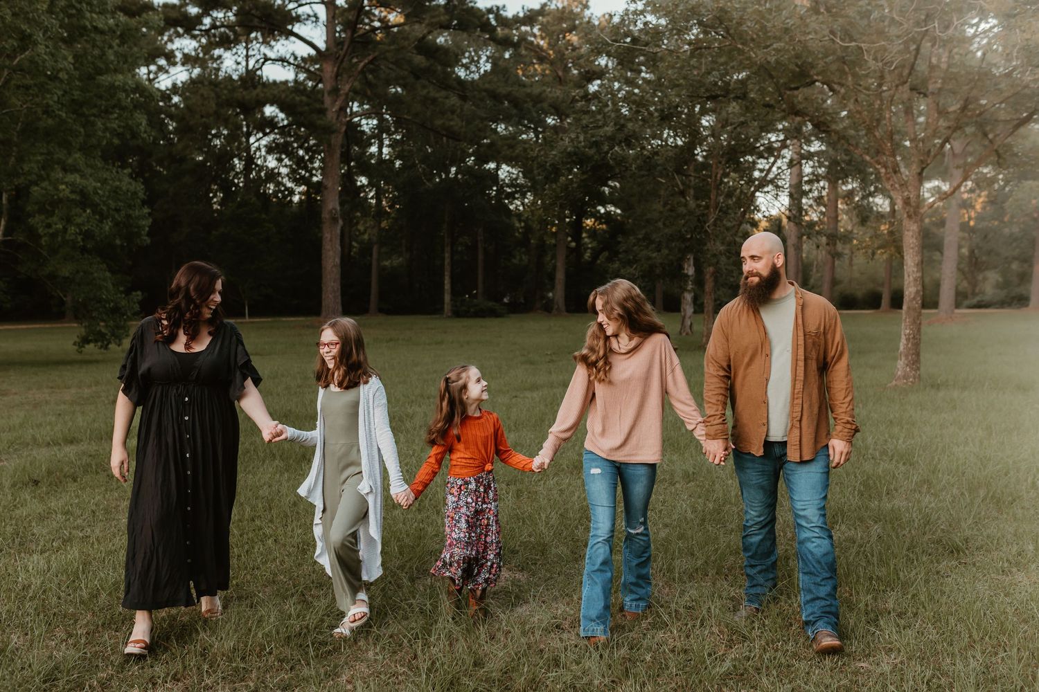 Family holding hands while walking together in a serene park setting.
