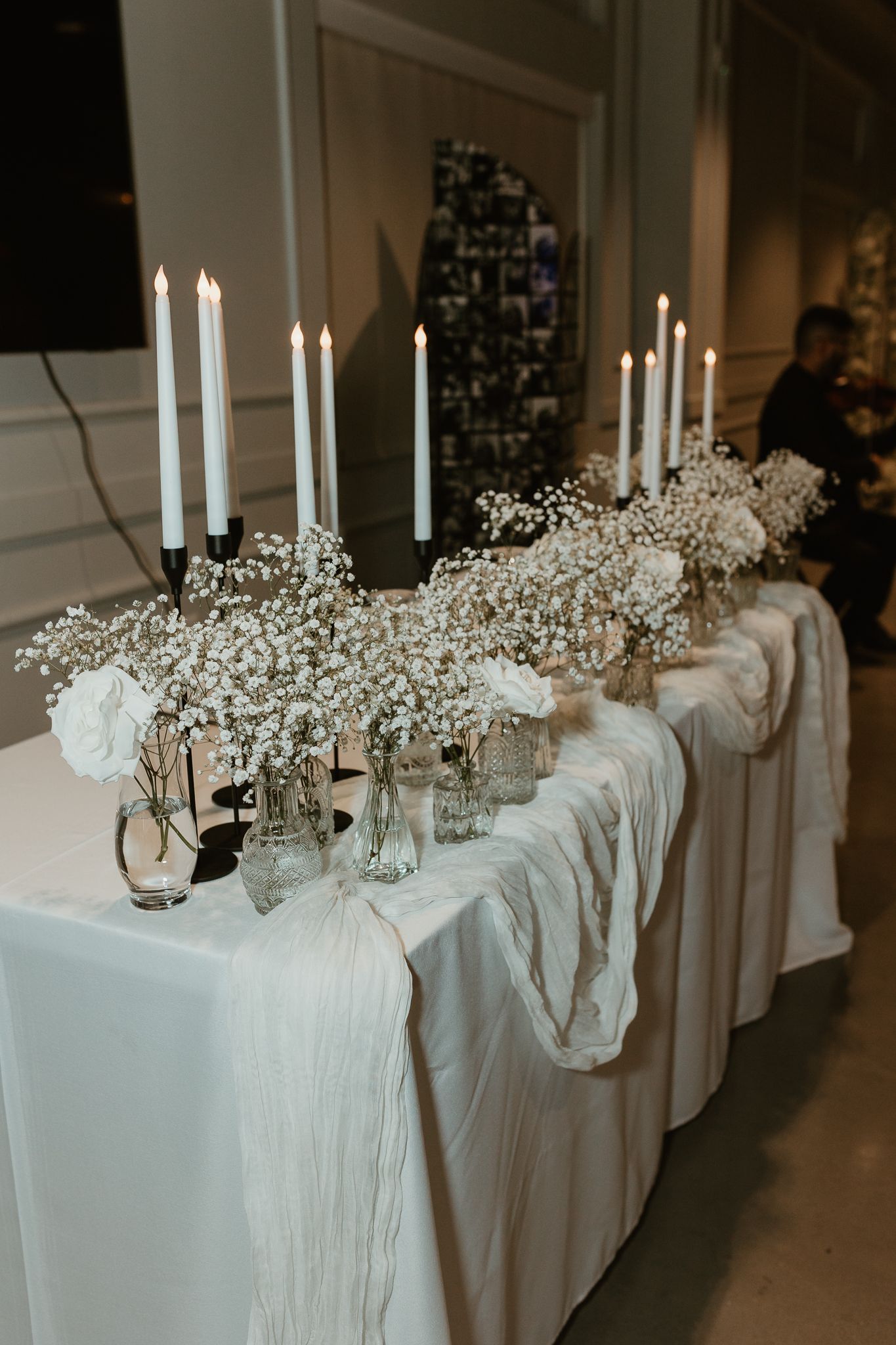 Elegant wedding reception table with white linens and tall white candles decorated with baby's breath flowers.