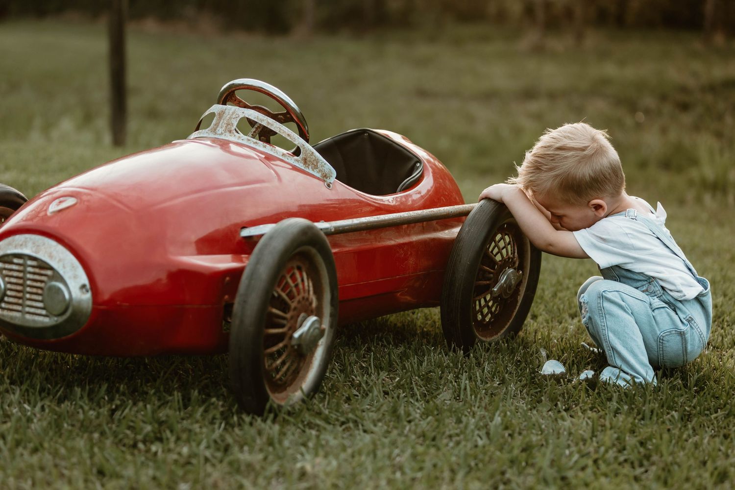 Red vintage pedal car photographed on grass during sunset.