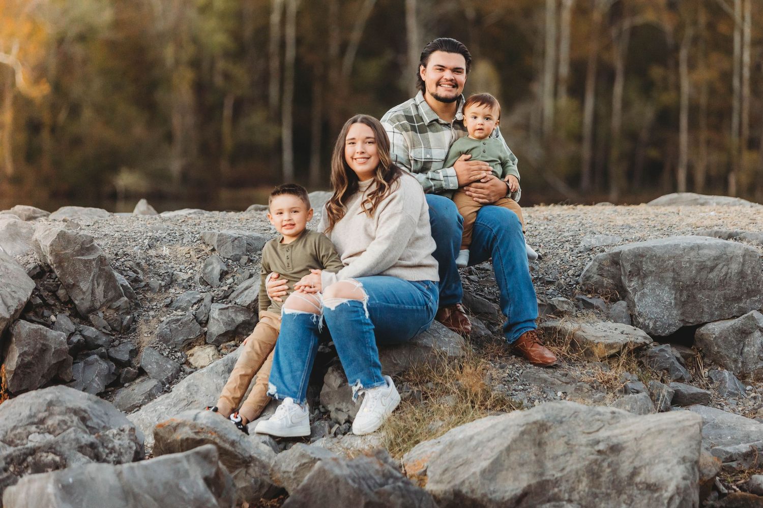 Family sitting together on large rocks by a lake during golden hour in autumn.